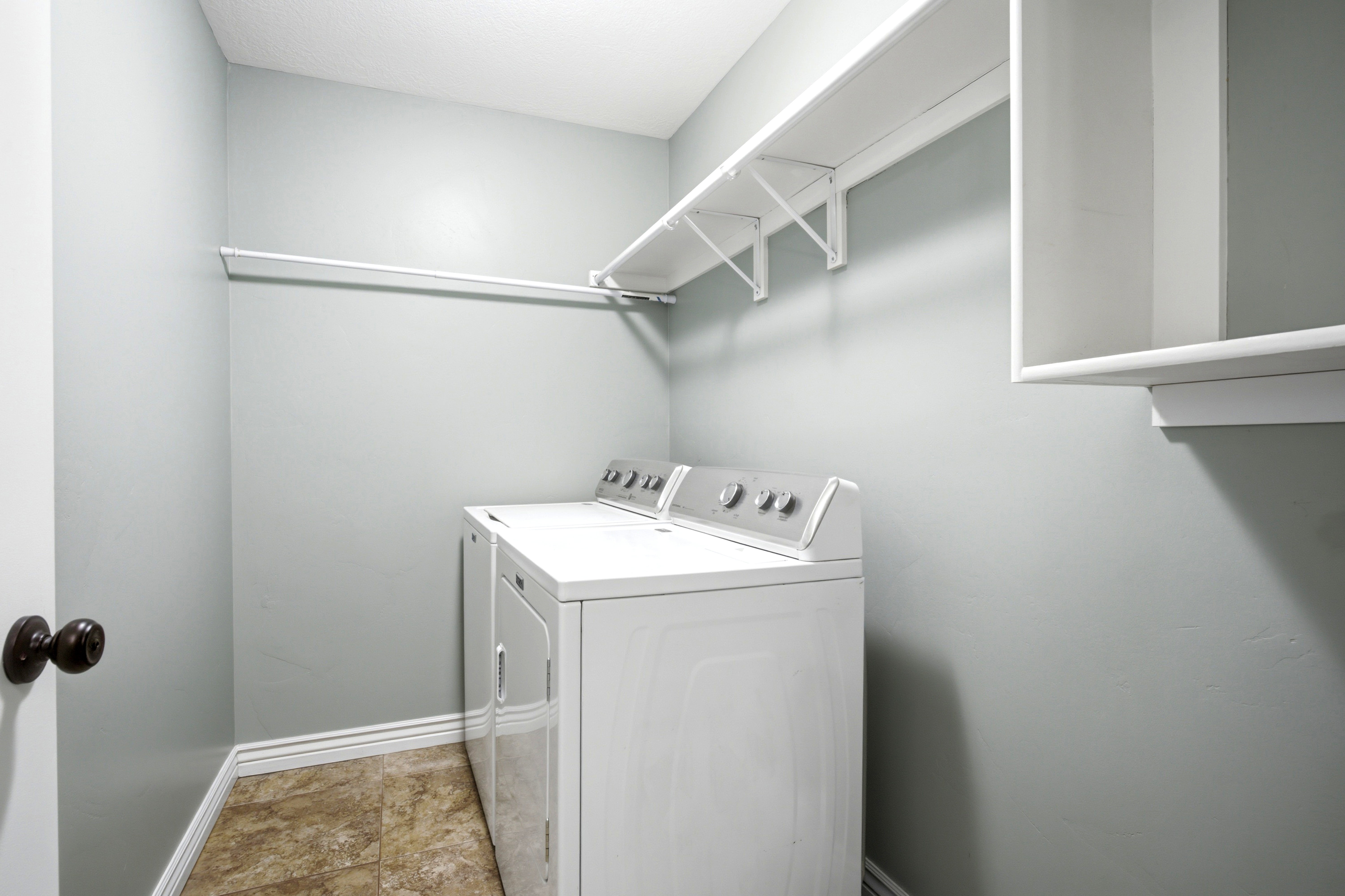 Laundry area featuring a top-load washer and dryer, wall-mounted shelving, and a hanging rod