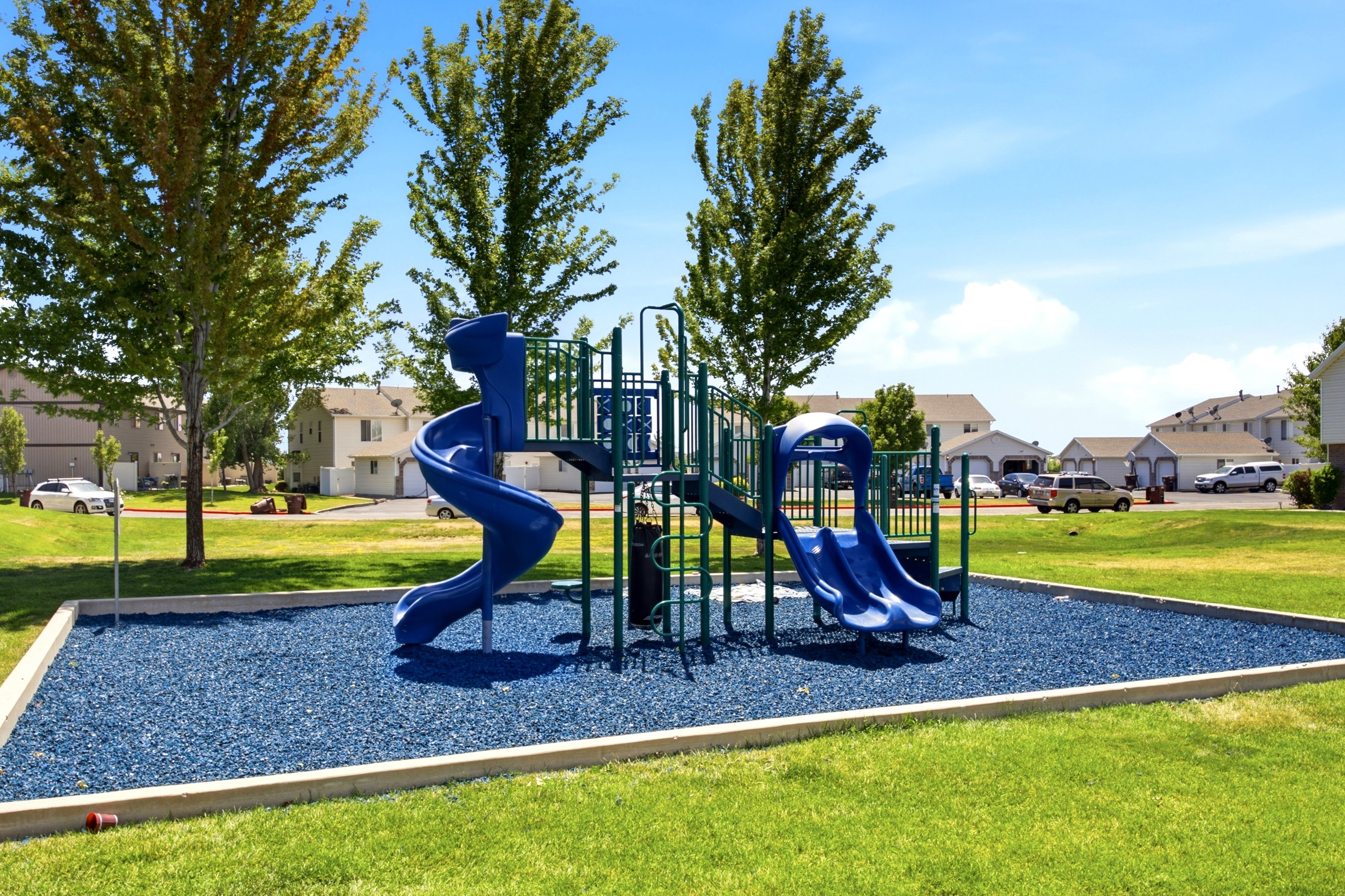 Outdoor play structure featuring multiple slides, climbing elements, and a blue rubberized ground surface