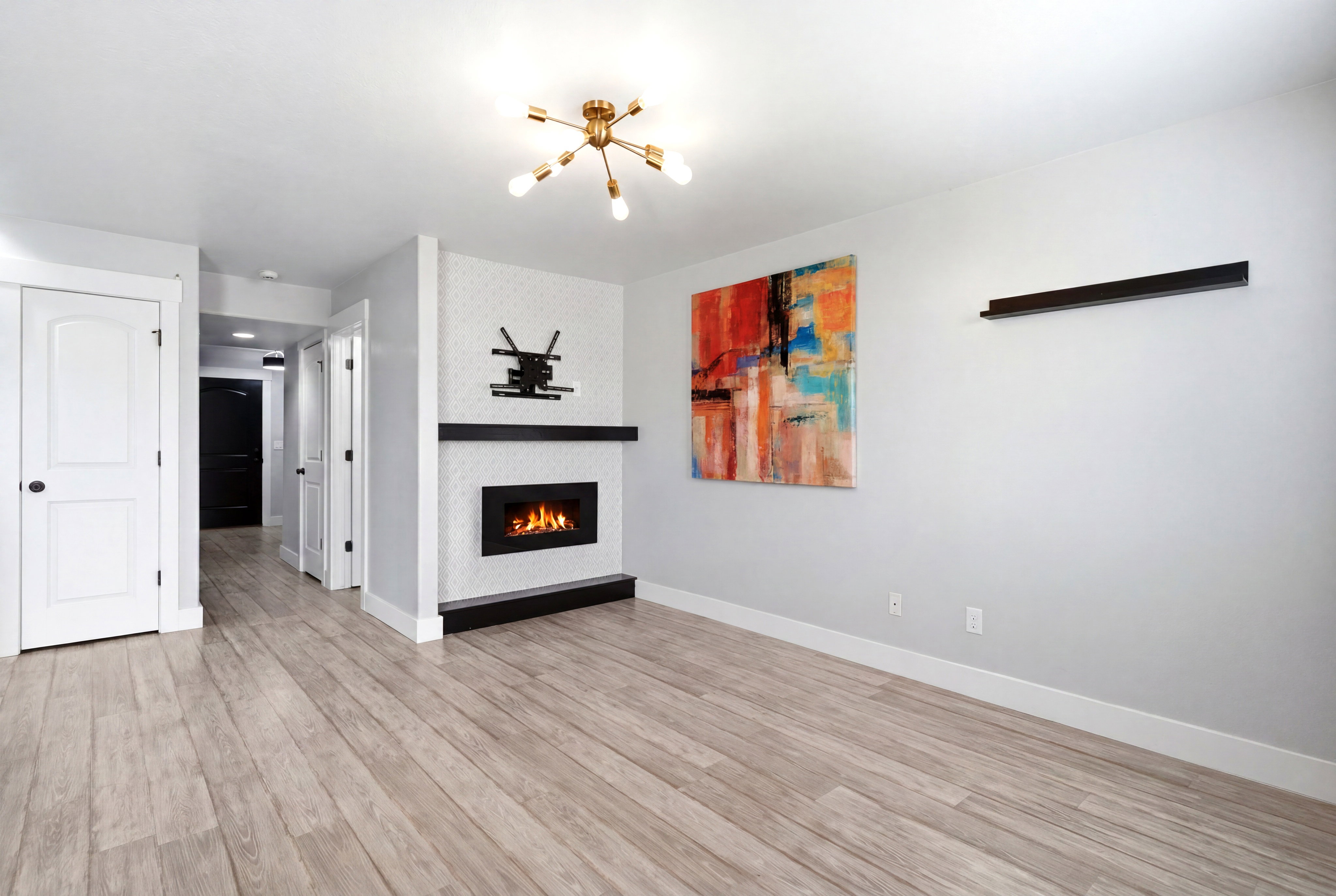 Open-concept living space featuring wood-finish flooring, a modern fireplace with a tiled surround, a black mantle, and a contemporary ceiling light fixture