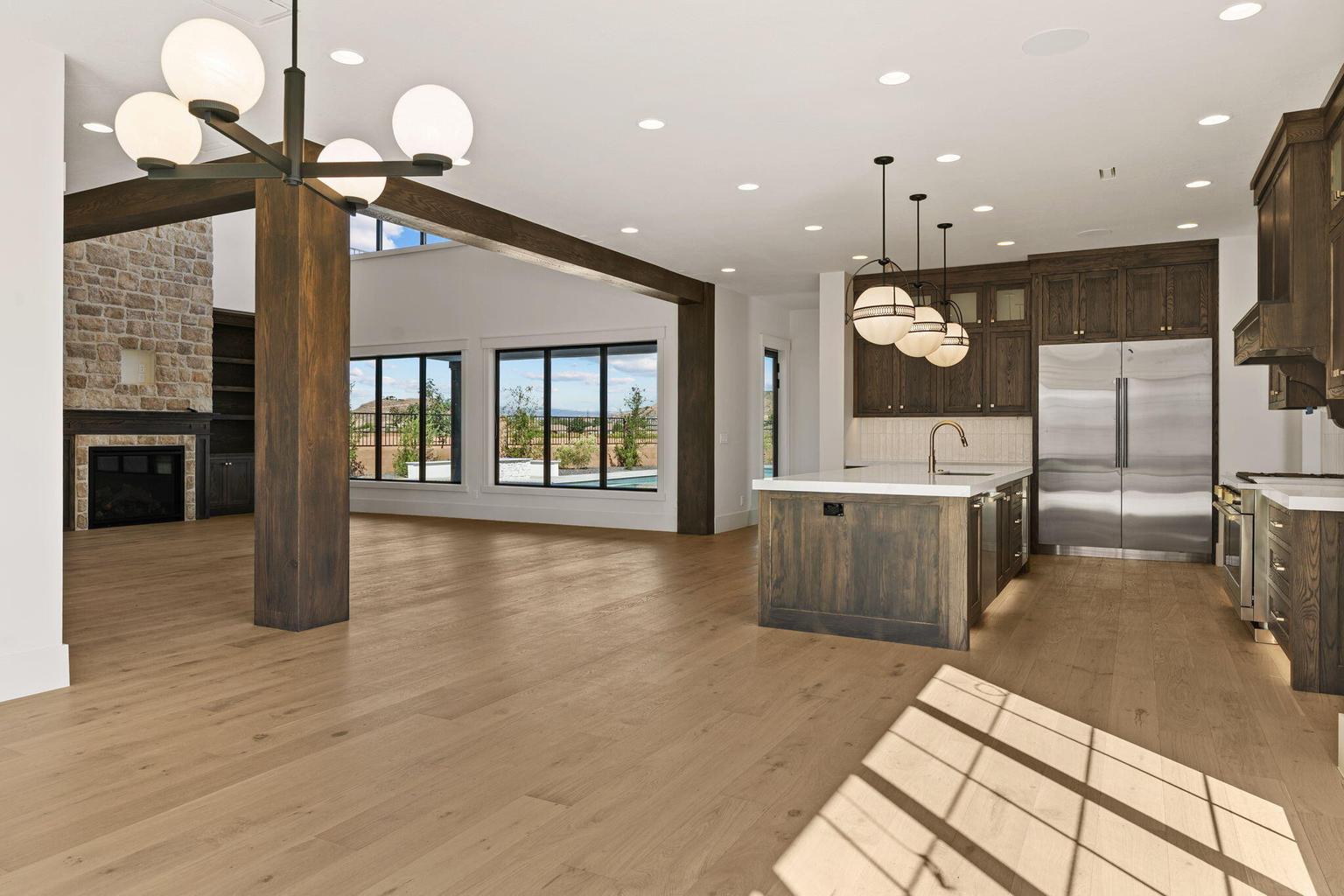 Open-concept living space featuring wood-finish flooring, a stone-faced fireplace, a vaulted ceiling with exposed wood beams, and large windows