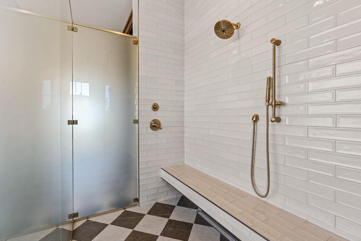 Walk-in shower with frosted glass enclosure, bronze-finish fixtures, white subway tile walls, built-in bench, and checkerboard floor tiling