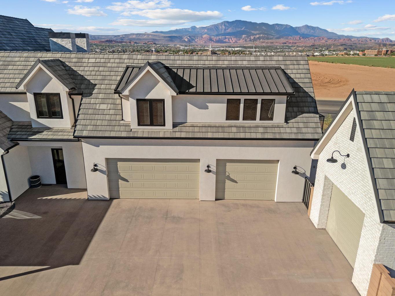 Multi-car garage and driveway featuring shaker-style garage doors, gooseneck lighting fixtures, and a white stucco and brick exterior