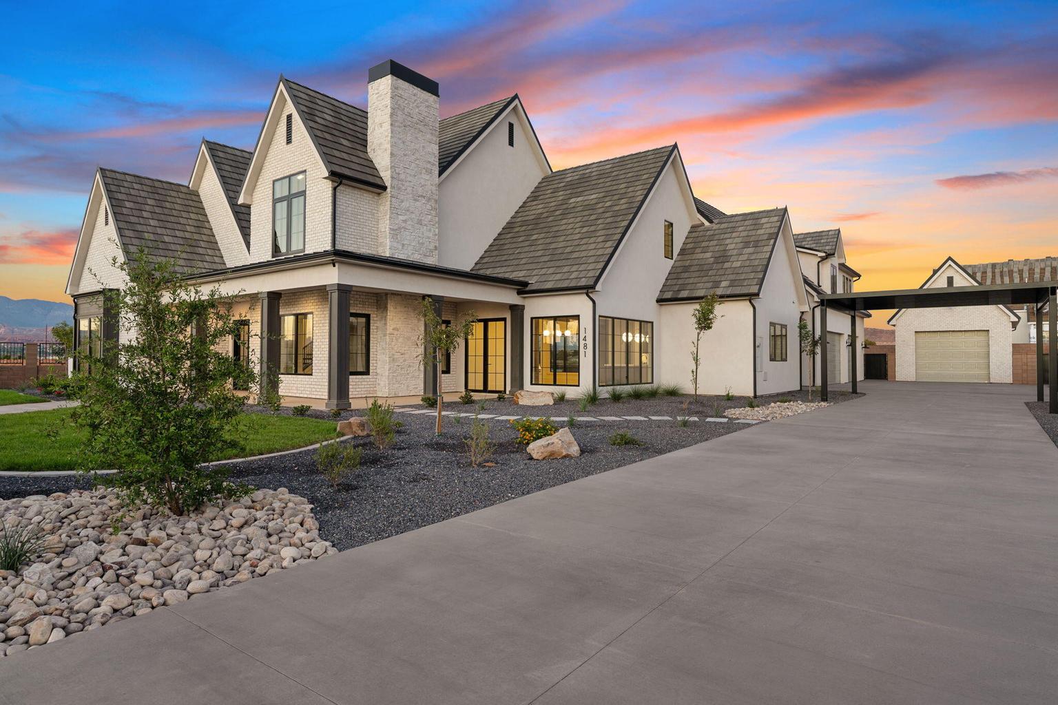 Modern farmhouse exterior with white stucco and brick accents, featuring multiple gables and a dark shingle roof