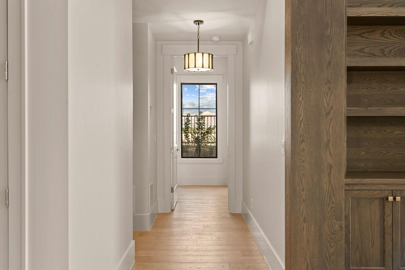 Hallway featuring light wood-finish flooring, white walls, and a large window with black grilles
