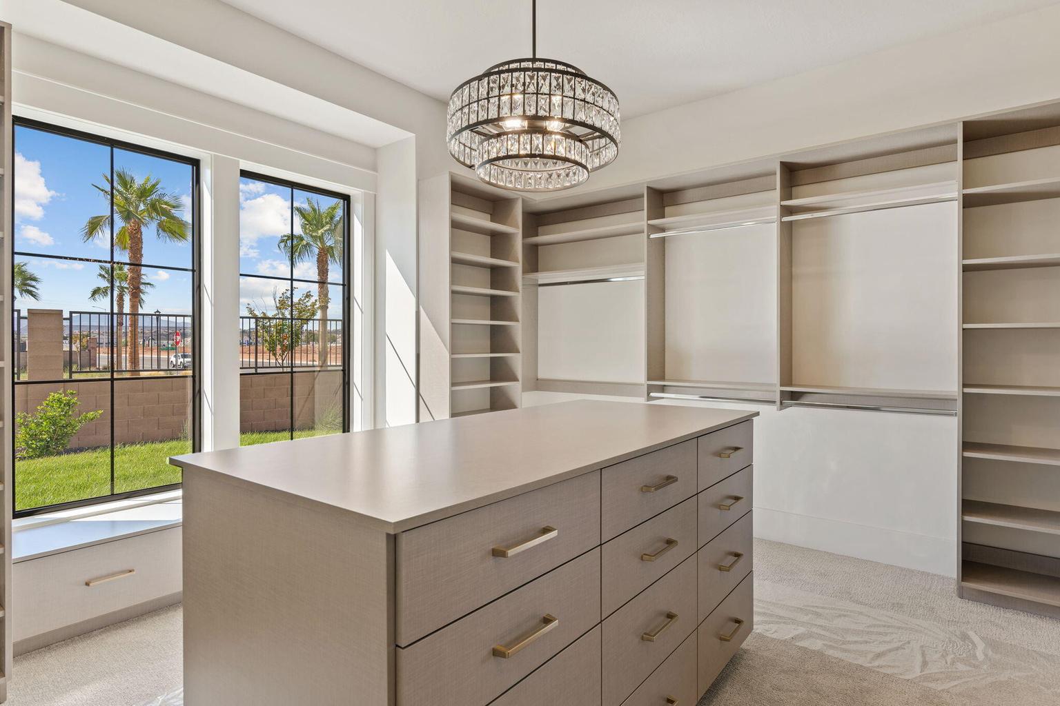 Spacious dressing room featuring an oval crystal chandelier, a large center island with drawers, integrated shelving, and multiple hanging rods