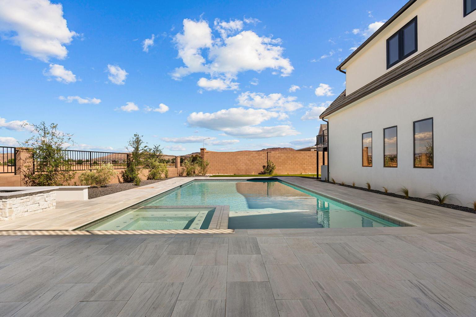 Expansive outdoor living area featuring a rectangular pool, integrated spa, and an adjacent fire pit with stone surround