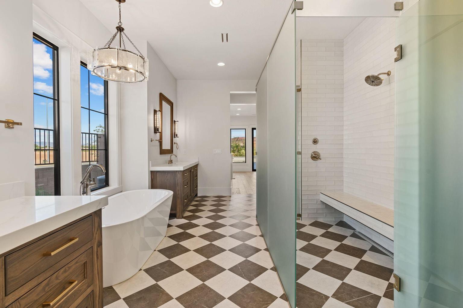 Spacious bathroom featuring a freestanding tub, dual vanities with quartz countertops, a large walk-in shower with bench seating, and patterned floor tiling