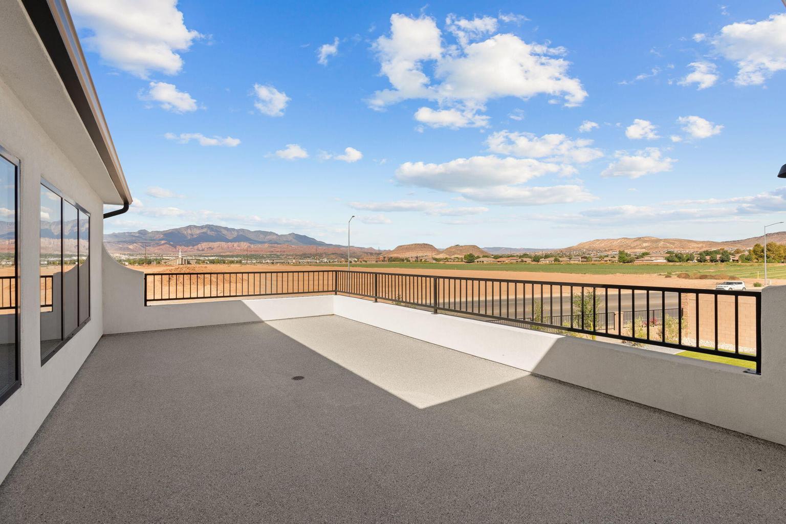 Spacious outdoor balcony featuring a textured concrete surface, black metal railings, and stucco perimeter walls