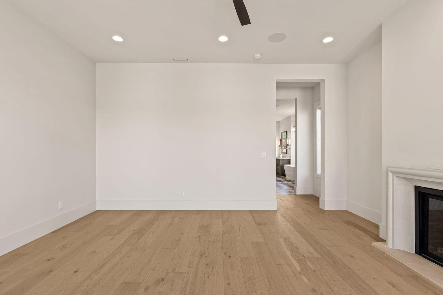Spacious room featuring light wood-finish flooring, recessed lighting, a ceiling fan, and a built-in fireplace with a stone mantel
