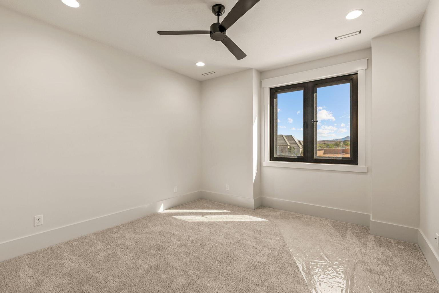 Bright room with a modern black ceiling fan, recessed lighting, and a large window featuring dark frames