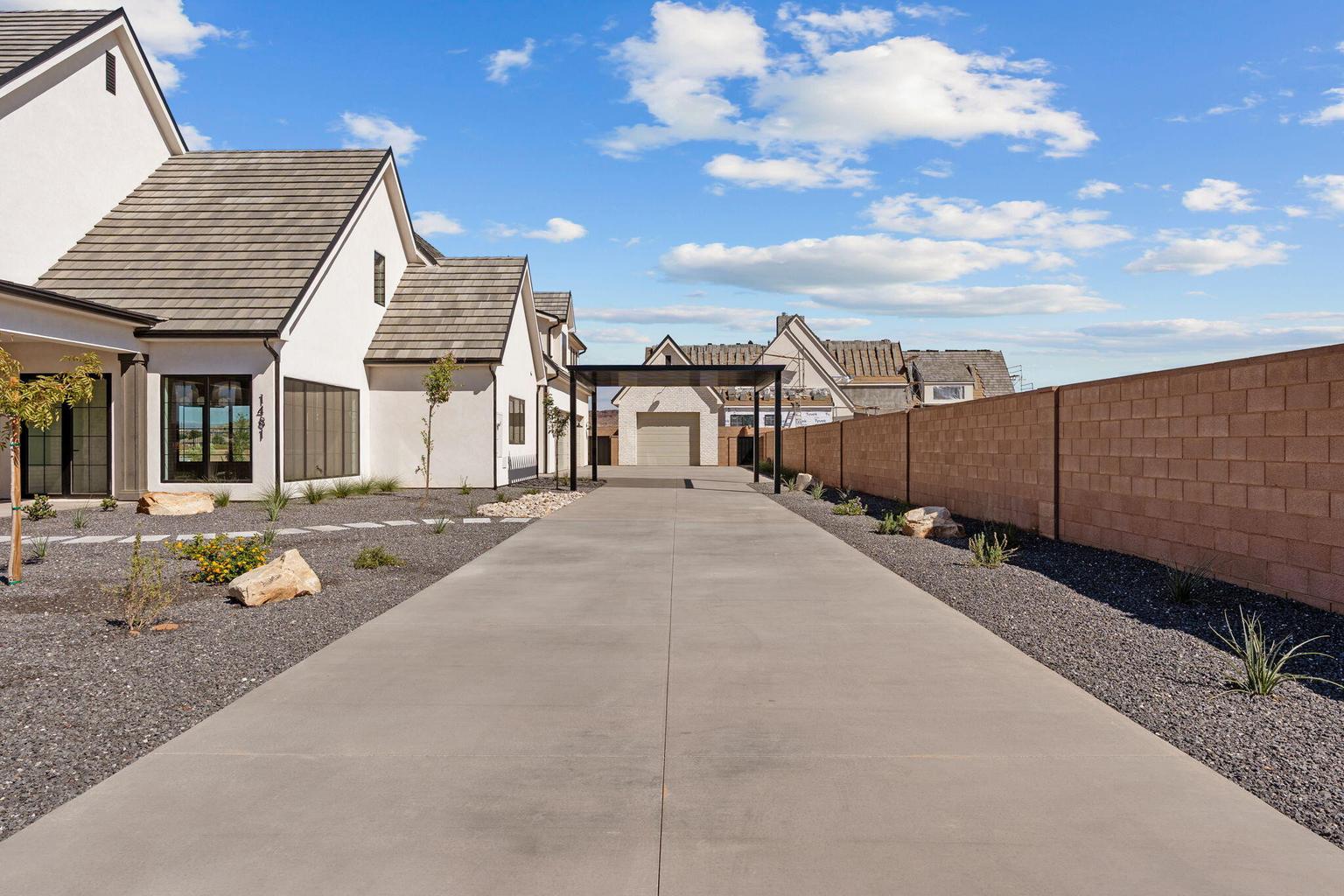 Long concrete driveway leading to a detached garage structure with a pergola