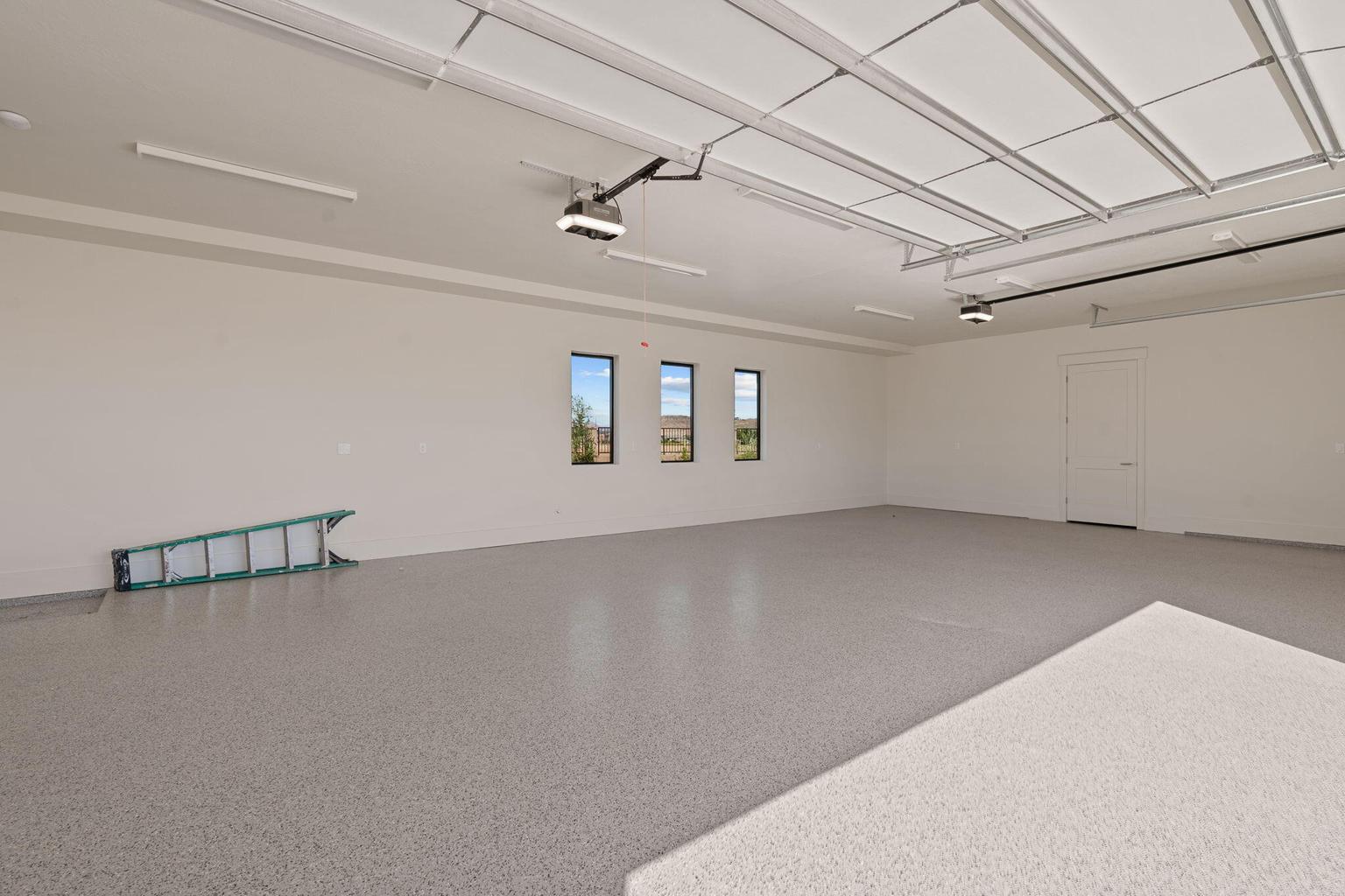 Spacious garage featuring a light-toned finished floor, multiple windows, and a side access door