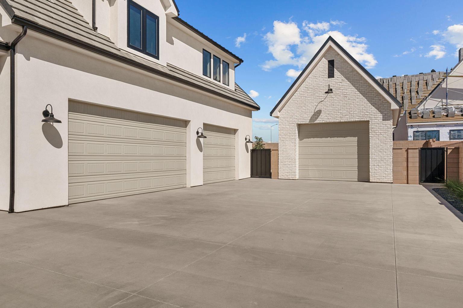 Expansive concrete driveway featuring three garage doors with a stucco-finished main structure and a brick-finished detached structure