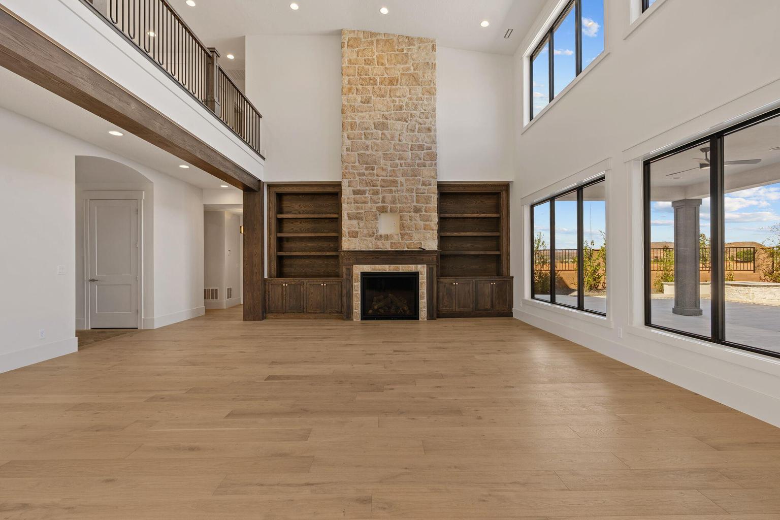 Spacious interior featuring a stone fireplace, built-in shelving, high ceilings, wood-finish flooring, and expansive windows