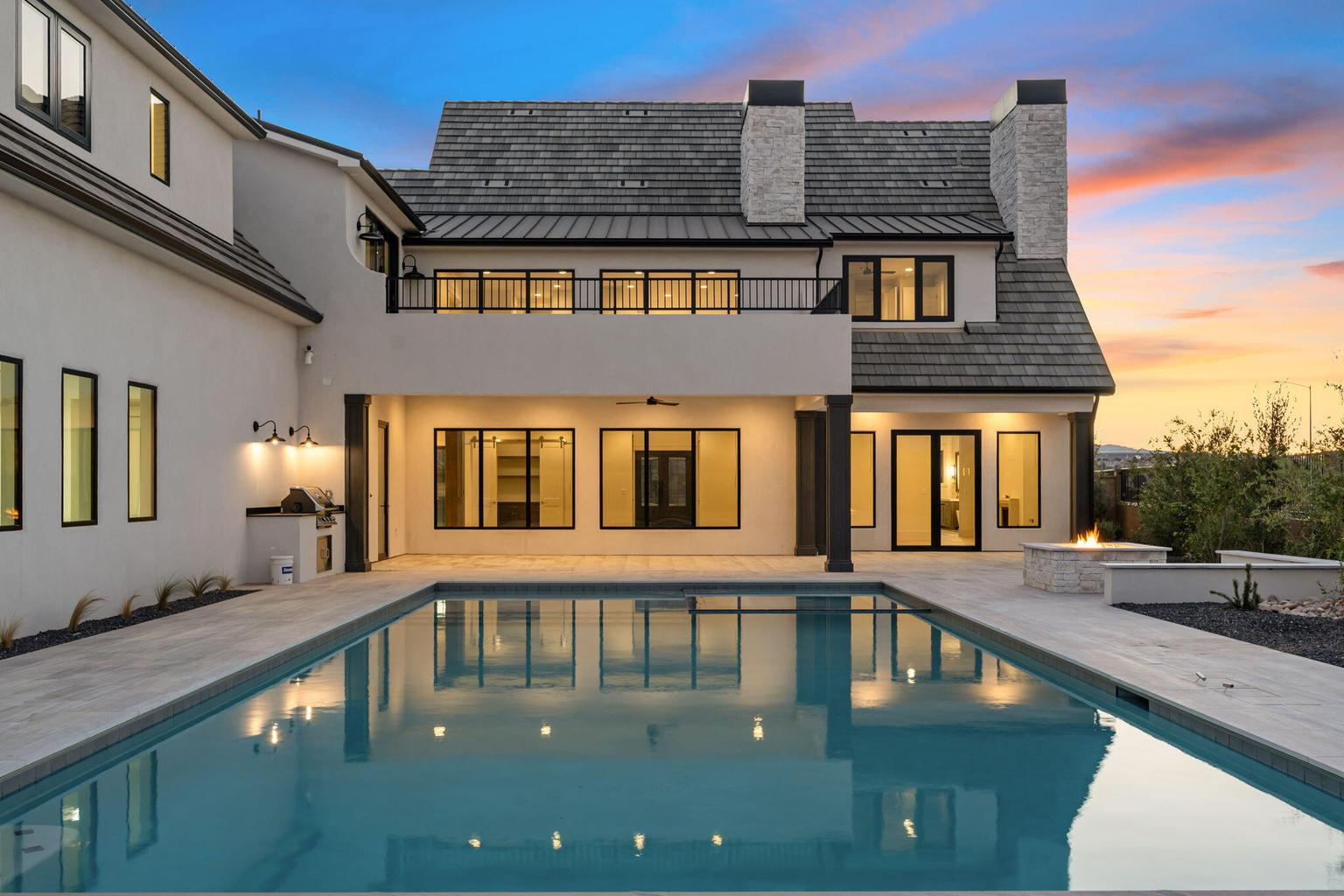 Expansive backyard oasis featuring a rectangular swimming pool, a built-in outdoor kitchen, an outdoor fire feature, and a second-story balcony
