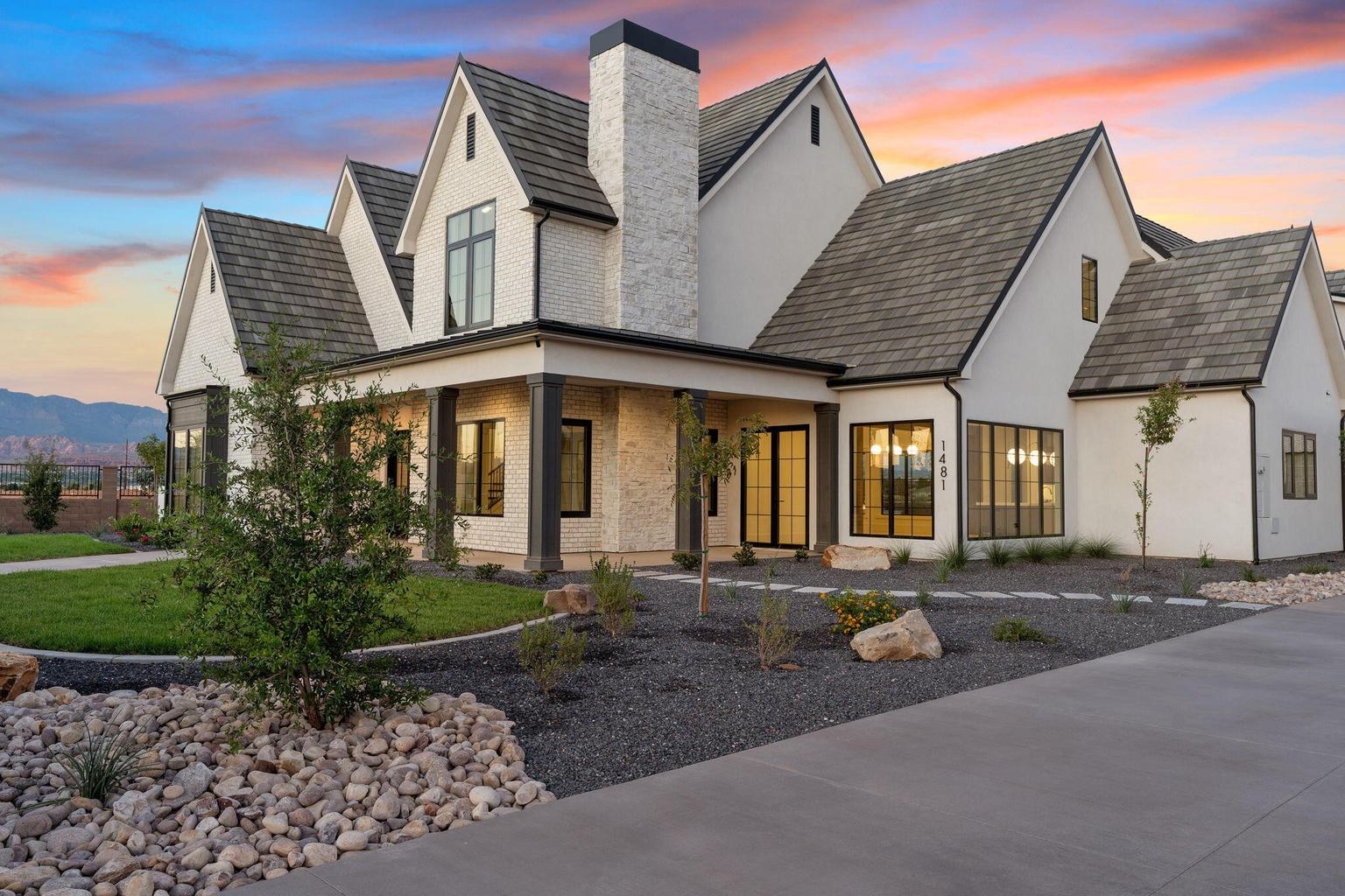 White stucco and stone exterior featuring a prominent stone chimney, multiple gables, dark-framed windows, and an inviting covered entry