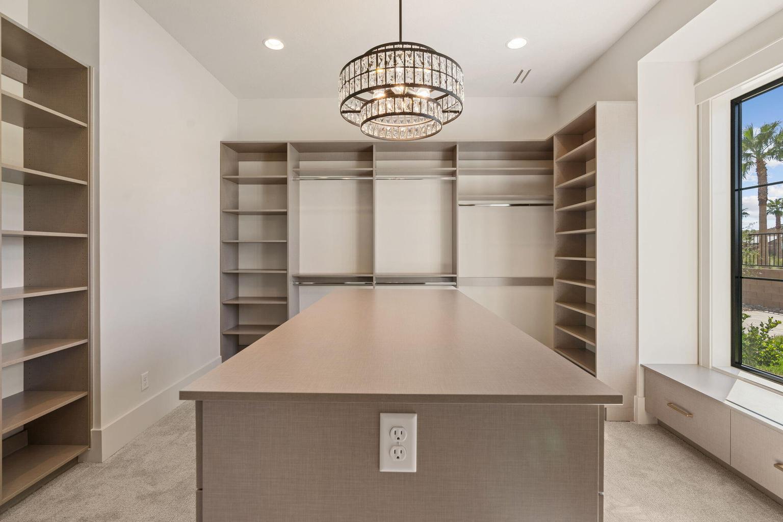 Spacious dressing room featuring a central island, extensive built-in shelving, integrated hanging rods, recessed lighting, and a crystal chandelier