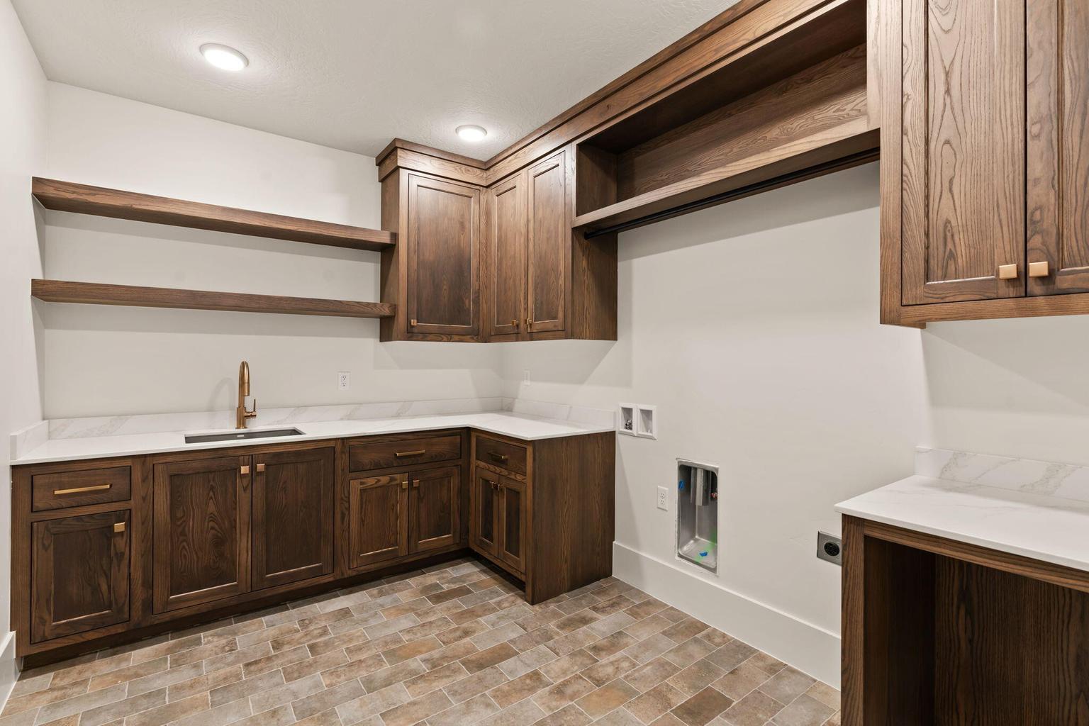 Laundry room featuring wood-finish cabinetry, white countertops, and a bronze-finish faucet