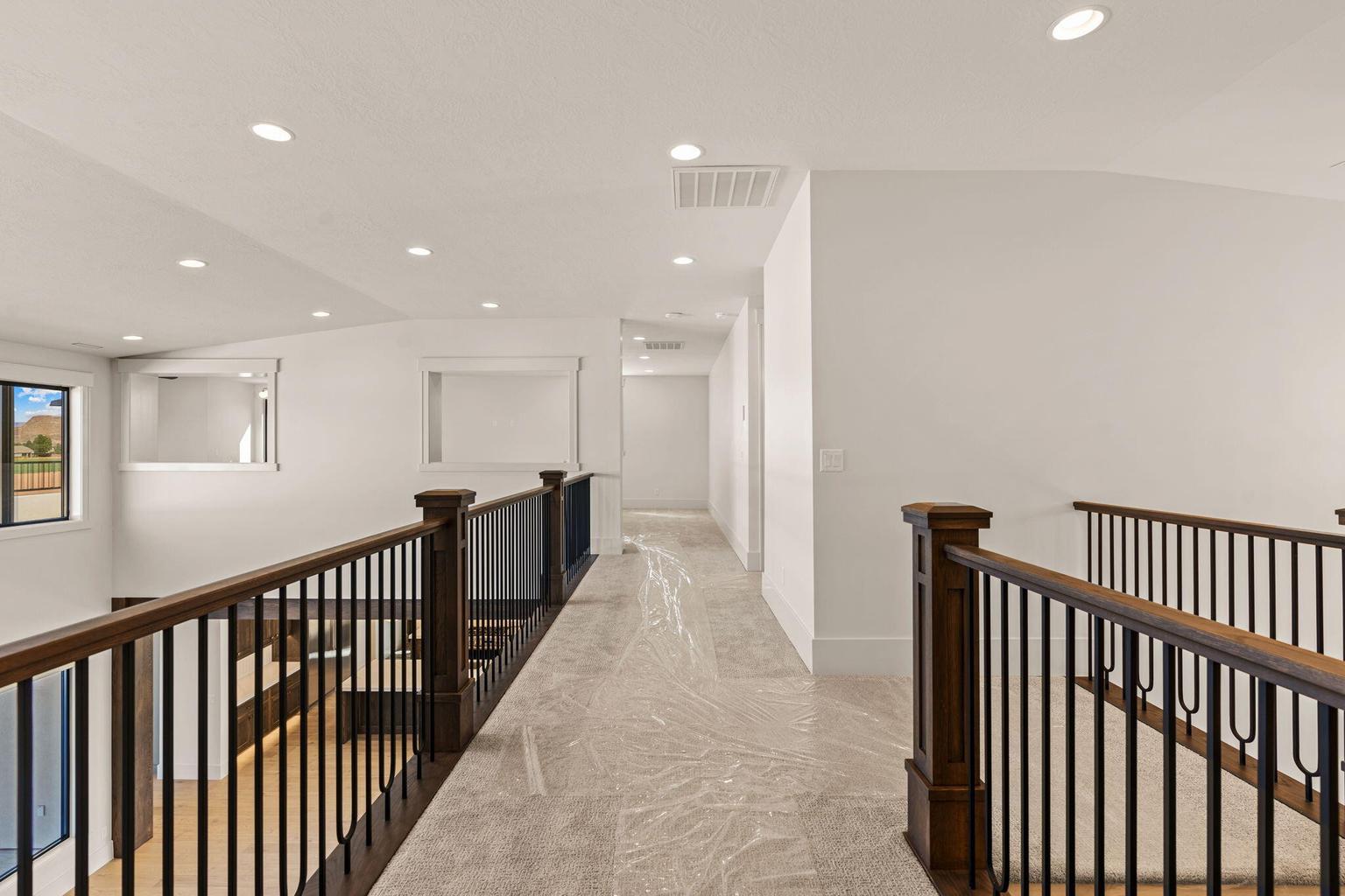 Upper-level hallway featuring recessed lighting, a carpeted floor, and dark wood railings with black iron balusters