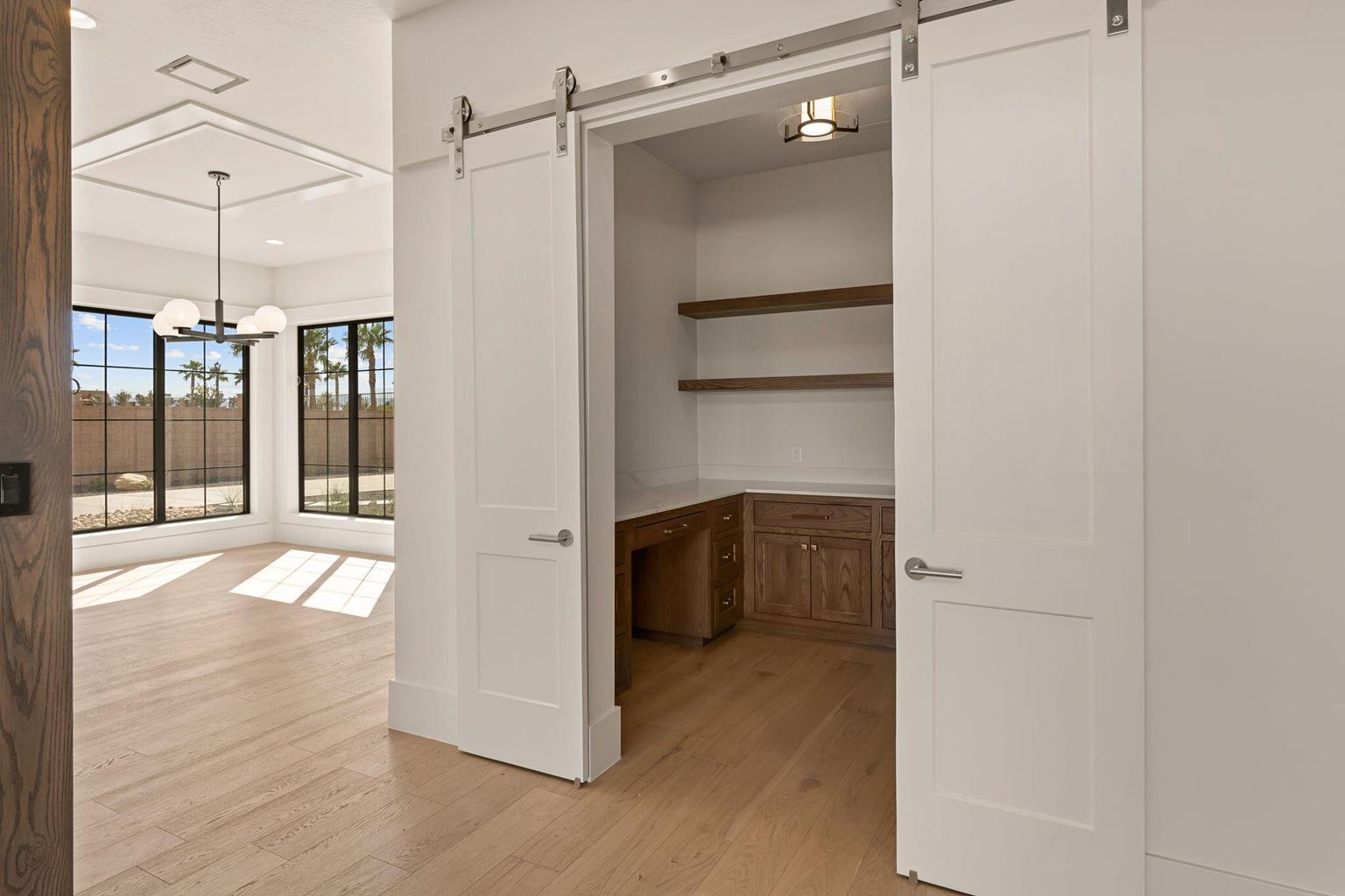 Interior office nook featuring barn doors, wood-finish flooring, built-in desk, floating shelves, and recessed lighting