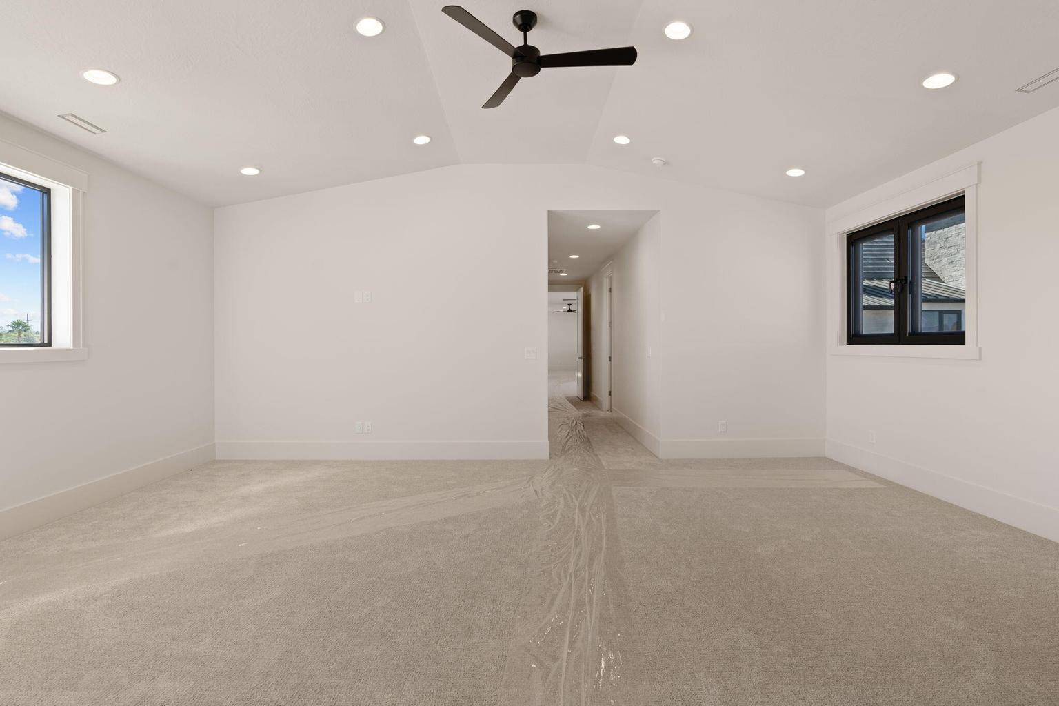Spacious room featuring vaulted ceilings, recessed lighting, a modern ceiling fan, two windows with black frames, and light-toned carpet flooring