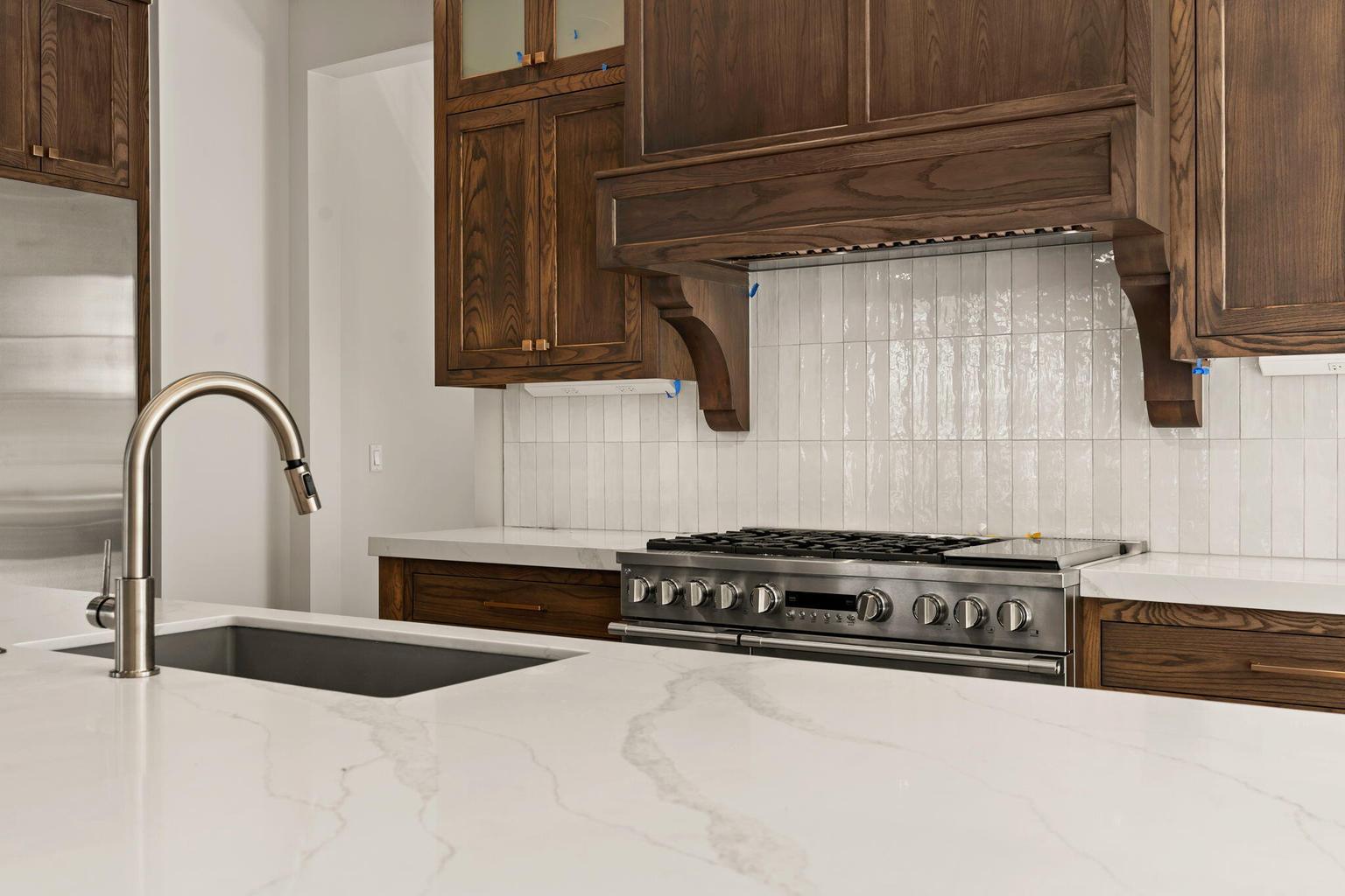 Kitchen featuring white countertops, an undermount sink with a gooseneck faucet, a stainless steel range, and wood cabinetry with a custom range hood