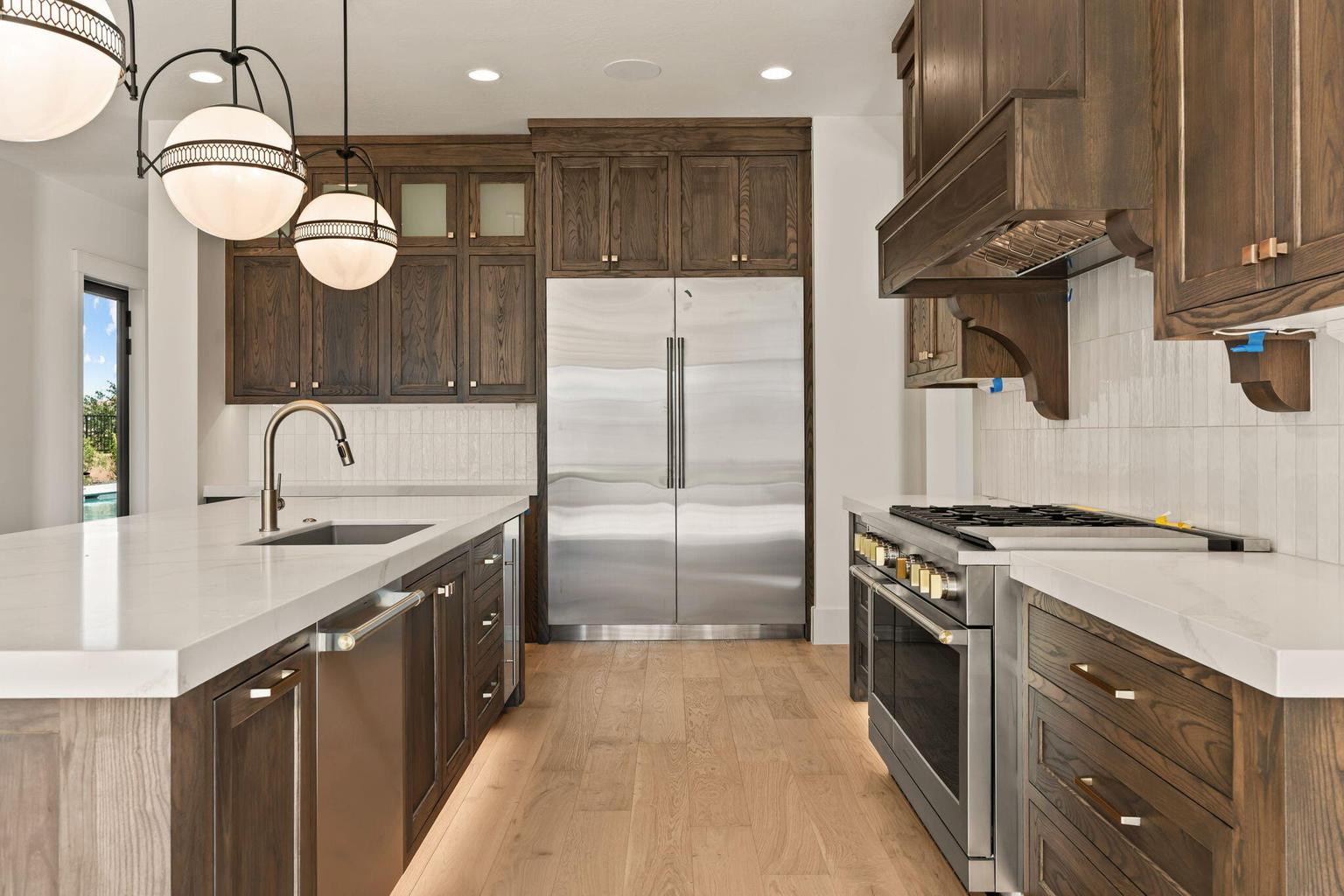 Gourmet kitchen featuring a large island with an undermount sink, quartz countertops, stainless steel appliances, dark wood-finish cabinetry, and wood-finish flooring