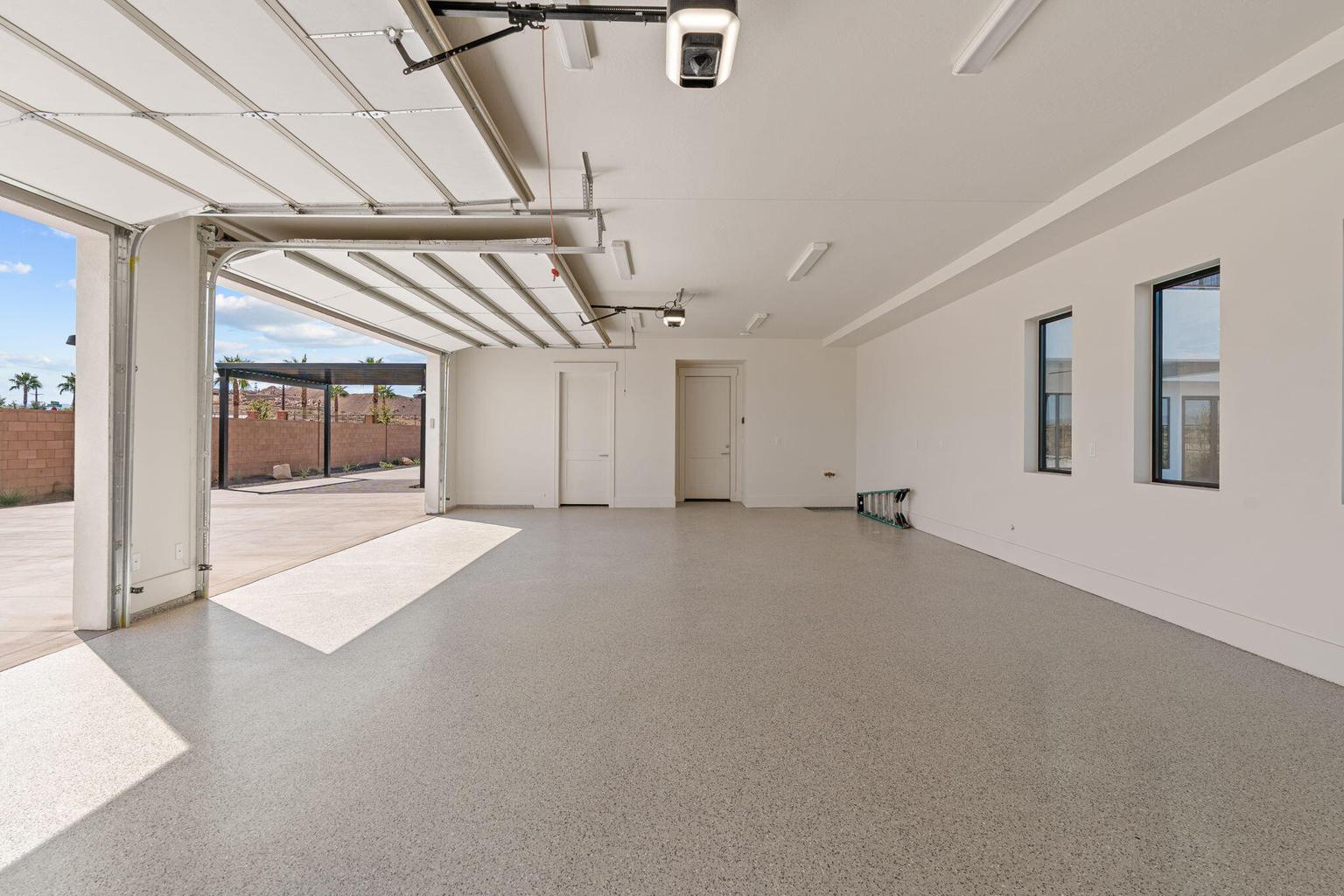 Spacious garage featuring a light-colored epoxy floor, multiple windows, a roll-up garage door, and recessed lighting