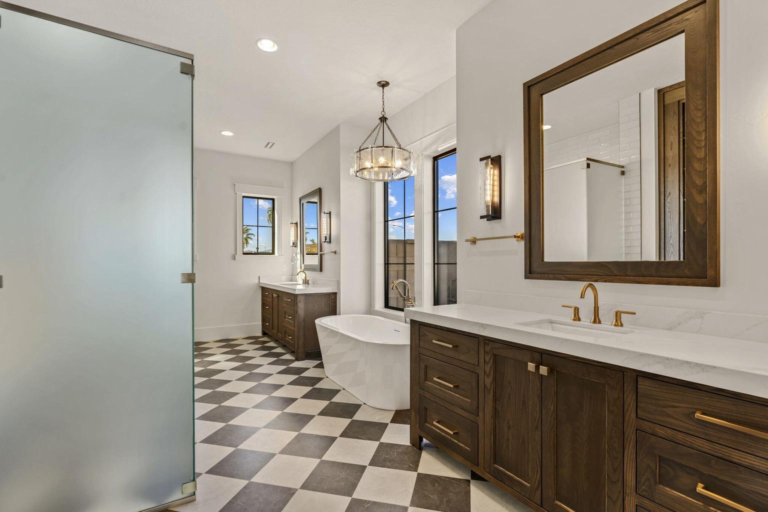Bathroom featuring a freestanding tub, dual wood-finish vanities with countertop sinks, a checkered tile floor, and a frosted glass shower enclosure