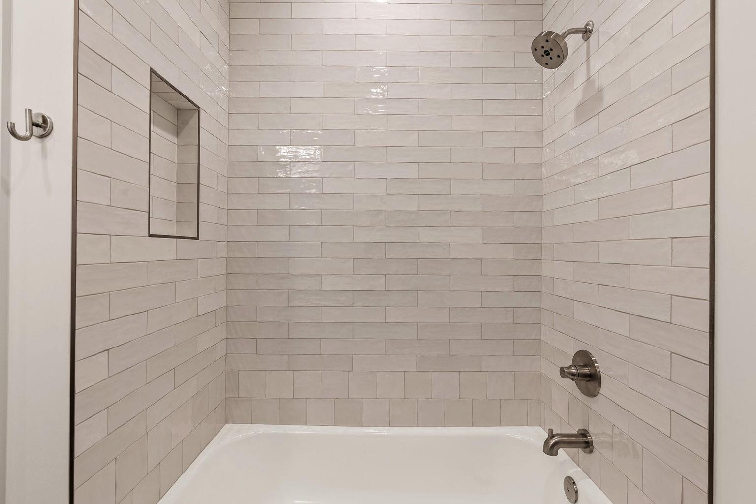 Bathtub with subway tile surround, recessed shower niche, and brushed nickel fixtures