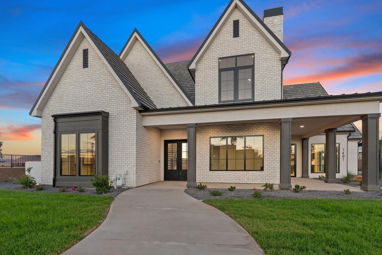 Modern farmhouse architectural style featuring white brick exterior, dark-framed windows, contrasting gables, a covered entry with dark columns, and a landscaped front yard with a curved concrete path