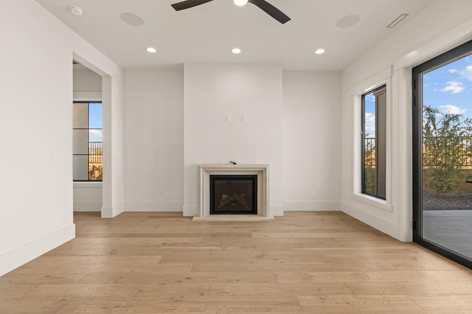 Bright interior space featuring light wood-finish flooring, a fireplace with a stone surround, recessed lighting, and a ceiling fan