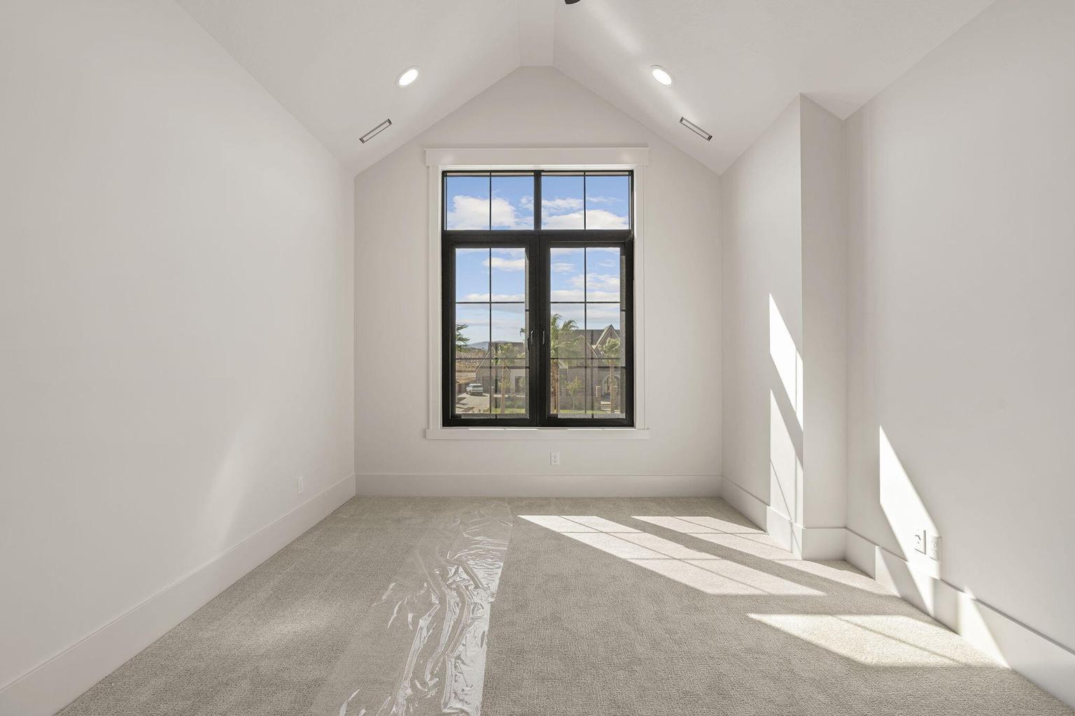 Vaulted ceiling with recessed lighting and a large black-framed window