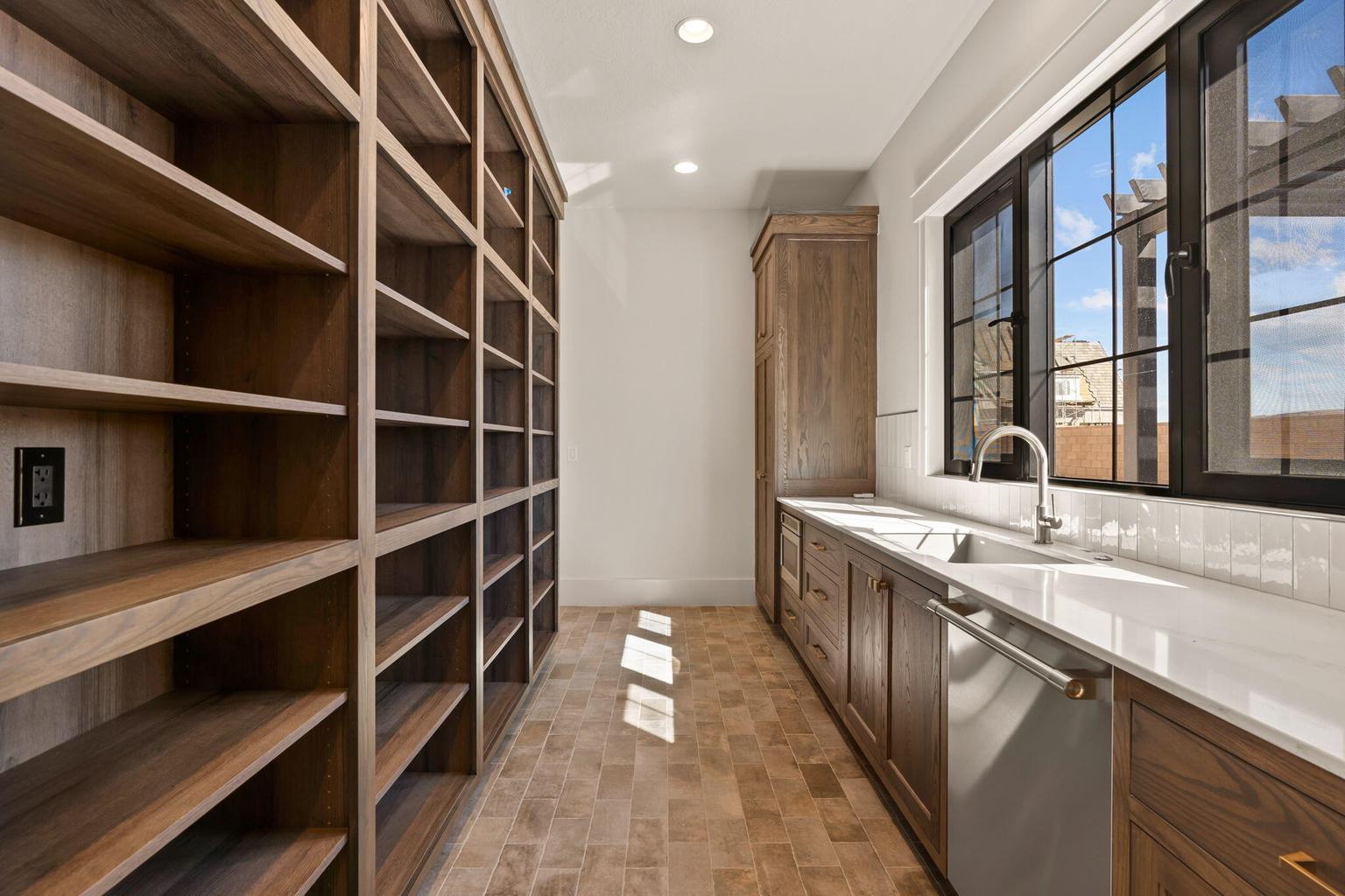 Extensive built-in wood shelving, a large black-framed window, and a stainless steel sink with a gooseneck faucet