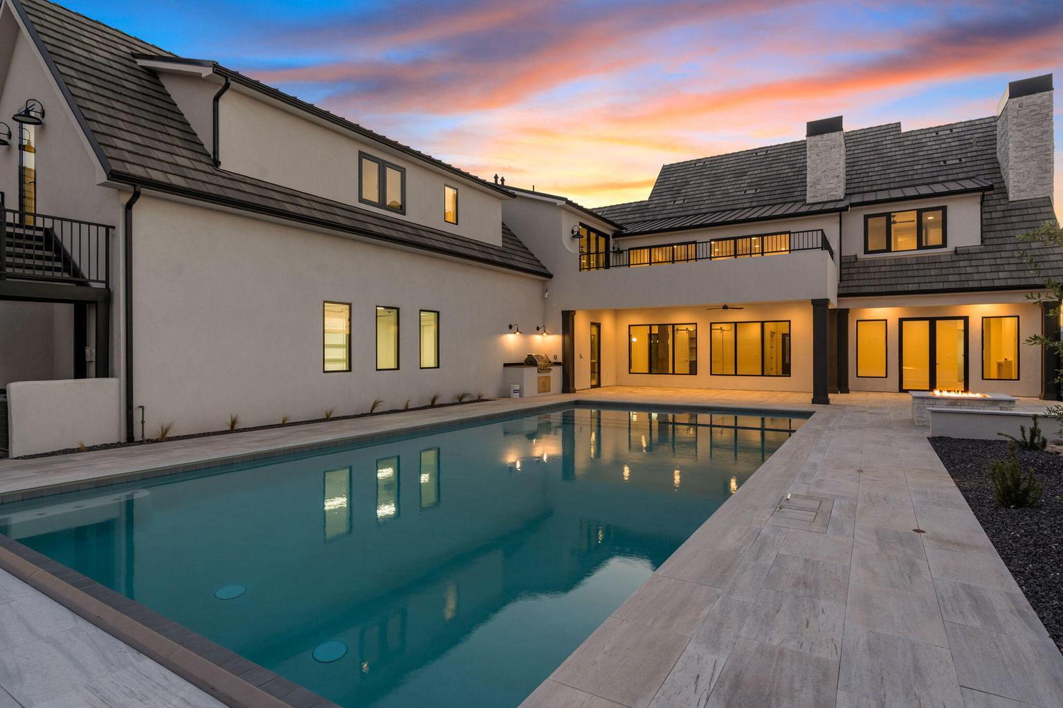 Expansive backyard featuring a rectangular swimming pool, light-toned paved patio, and a built-in fire pit