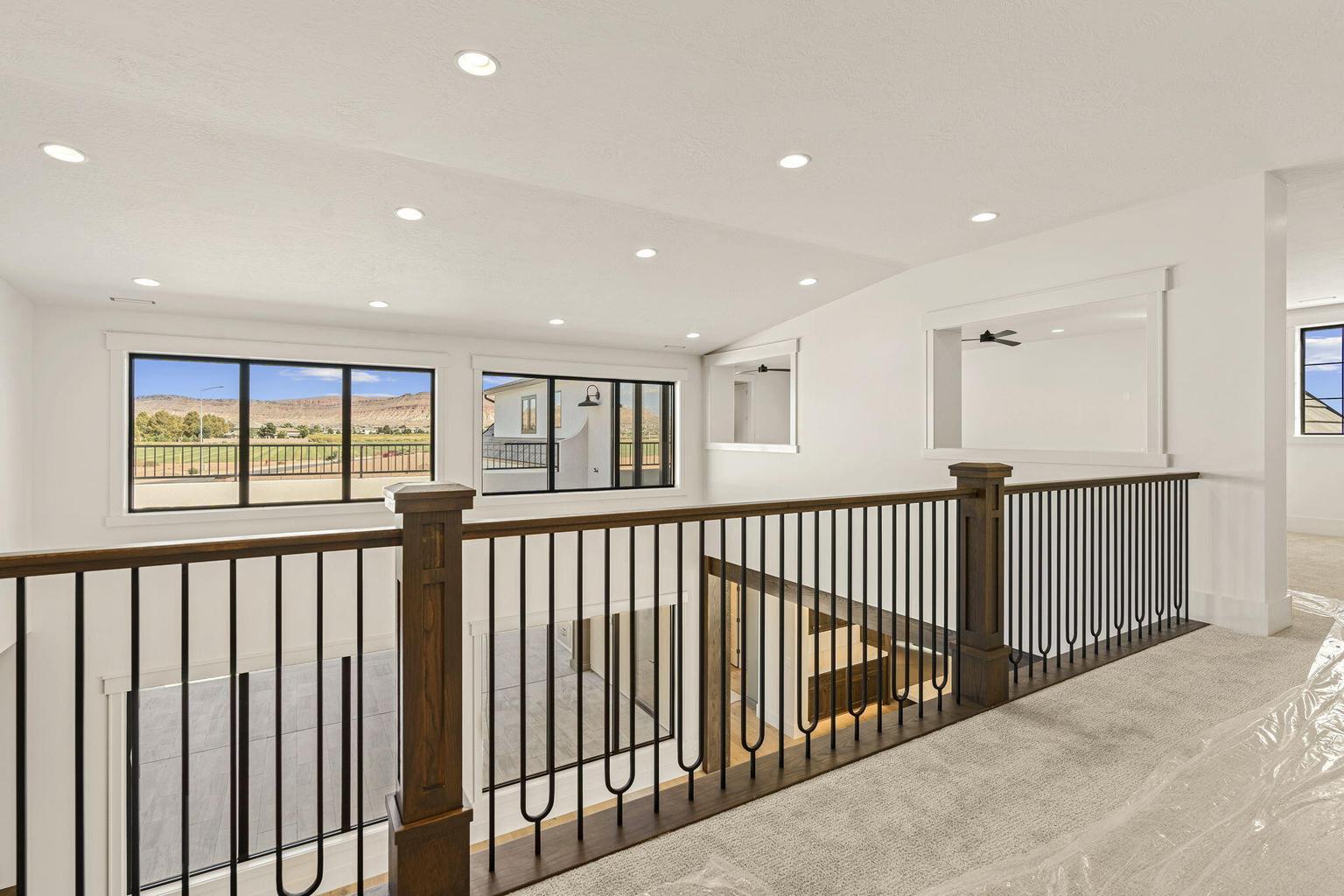 Upper-level landing featuring a wood-finish and wrought iron railing, recessed lighting, expansive windows with mountain scenery, and light-toned carpeting