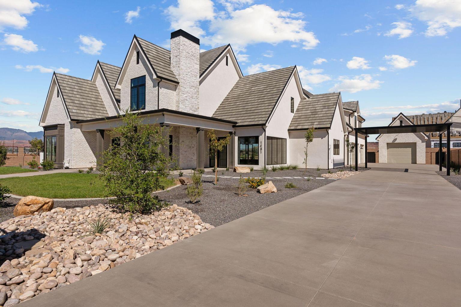 Contemporary white stucco exterior with multiple gables, a prominent chimney, dark-framed windows, and an extensive concrete driveway leading to a detached garage