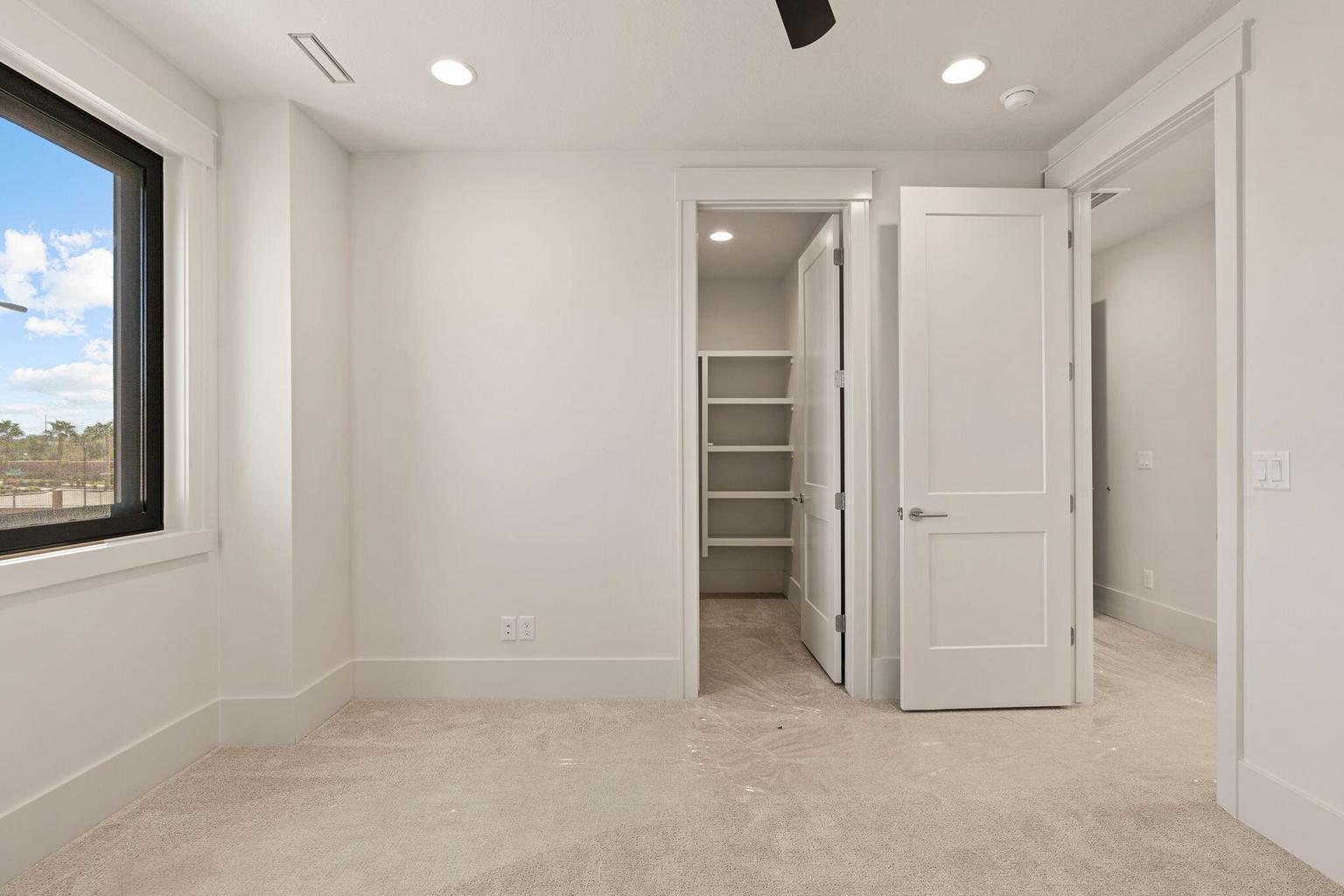 Carpeted room featuring a large window with black trim, recessed lighting, white baseboards, and a walk-in closet with built-in shelving