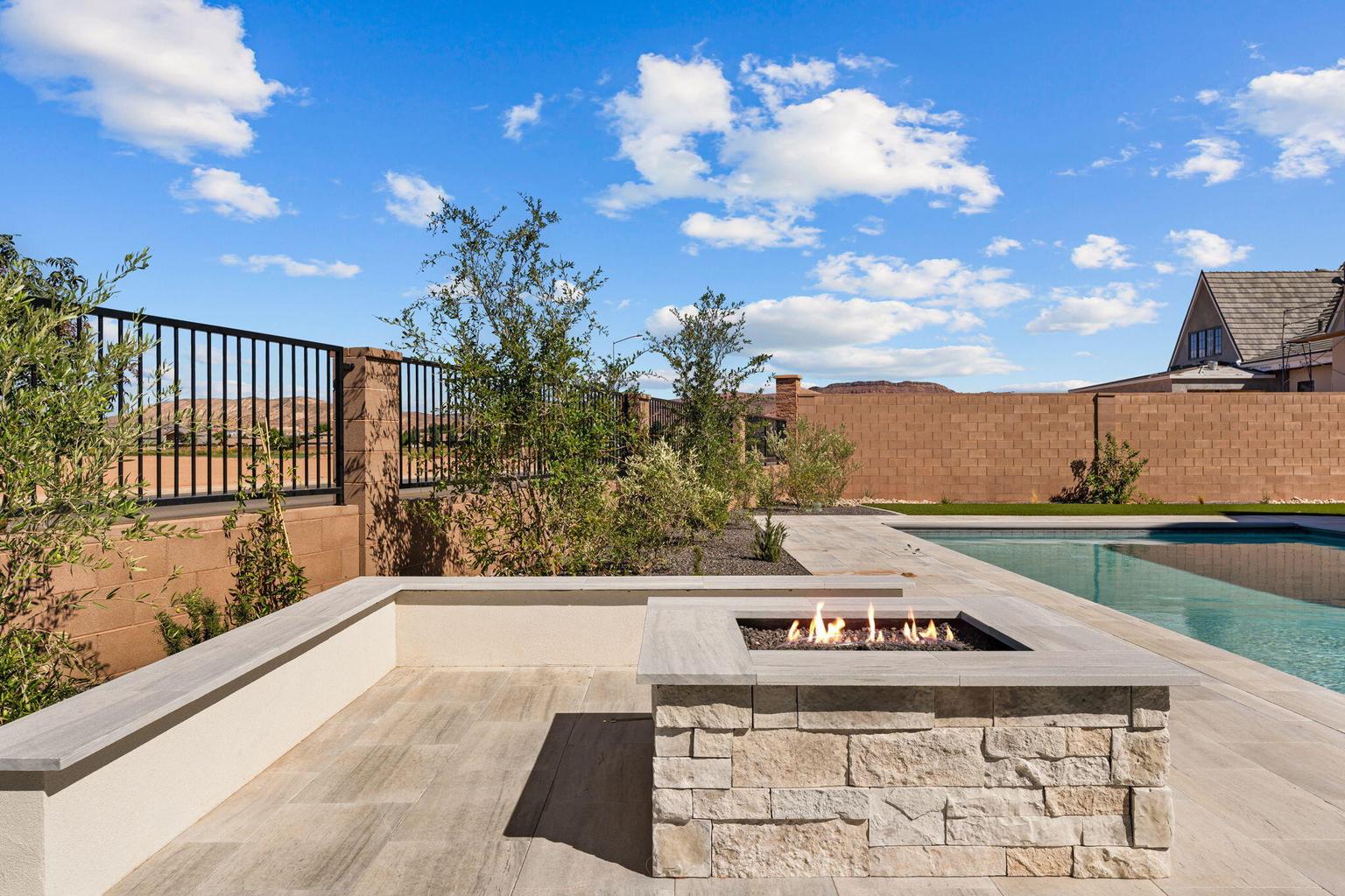 Outdoor living space featuring a built-in stone fire pit, extensive patio with light-toned tile, and an integrated swimming pool