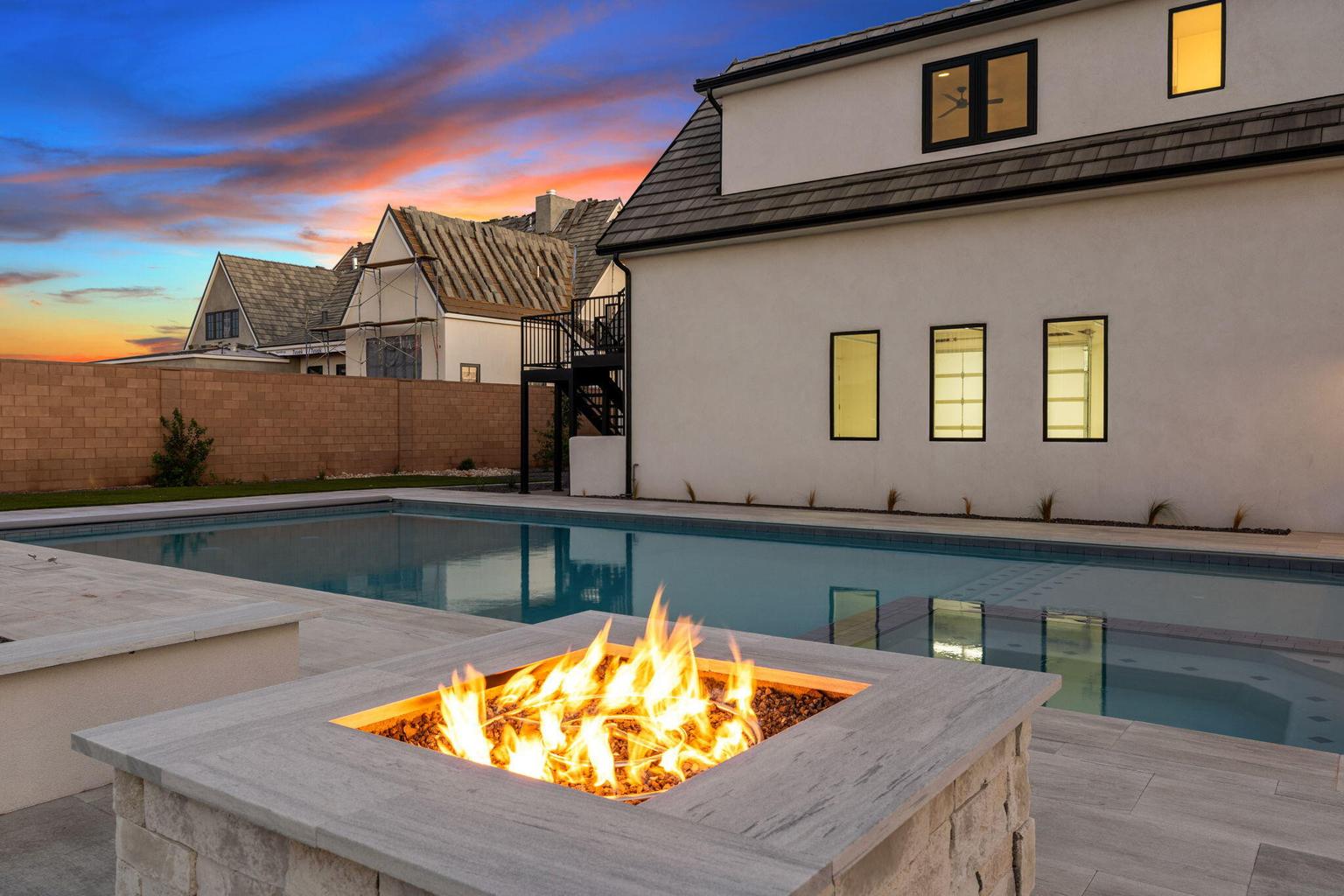 Fire pit with a stone veneer base and a square concrete cap, positioned alongside a rectangular swimming pool with a Baja shelf