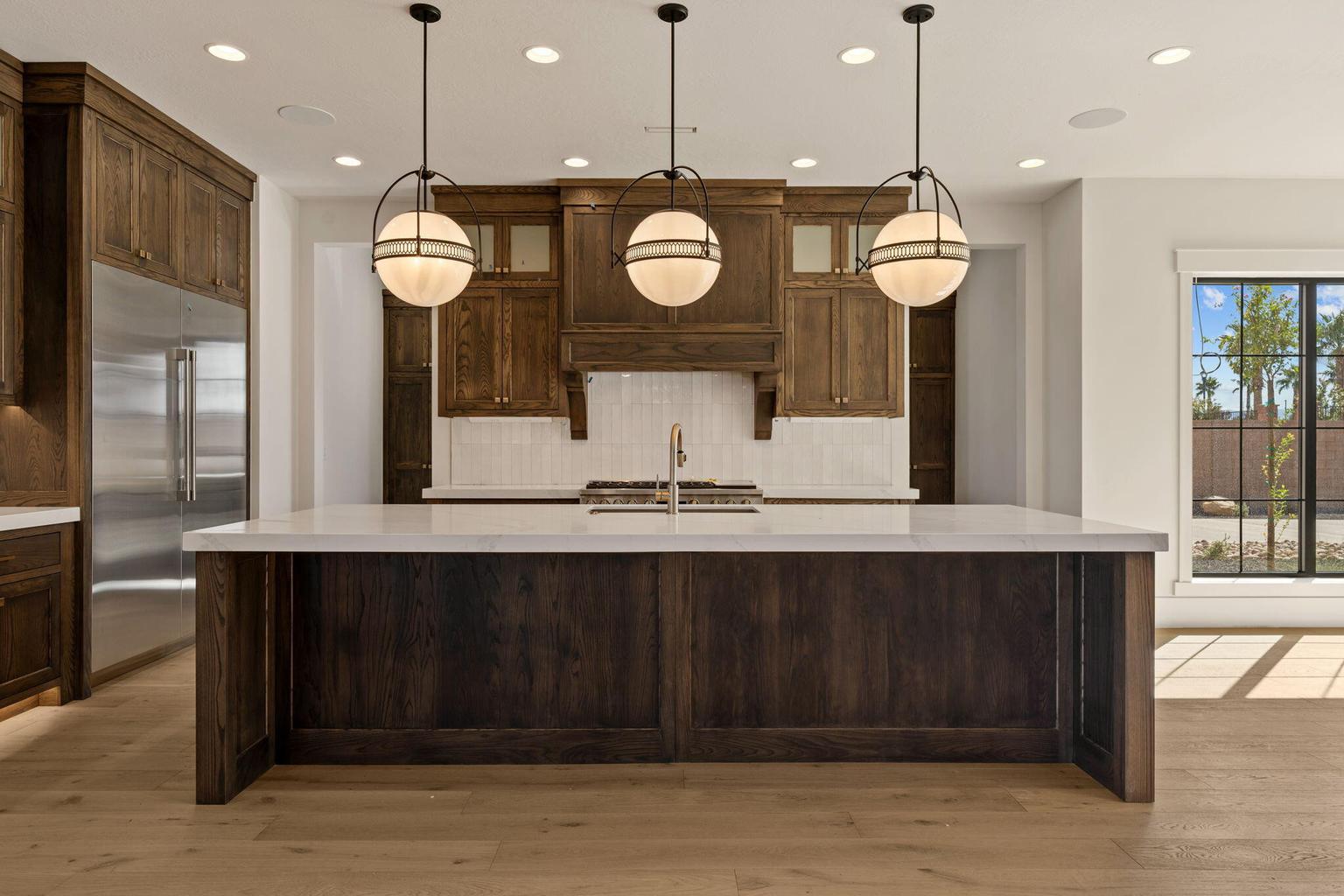 Kitchen featuring a large central island with a light-toned countertop, three globe pendant lights, dark wood cabinetry, a subway tile backsplash, and wood-finish flooring