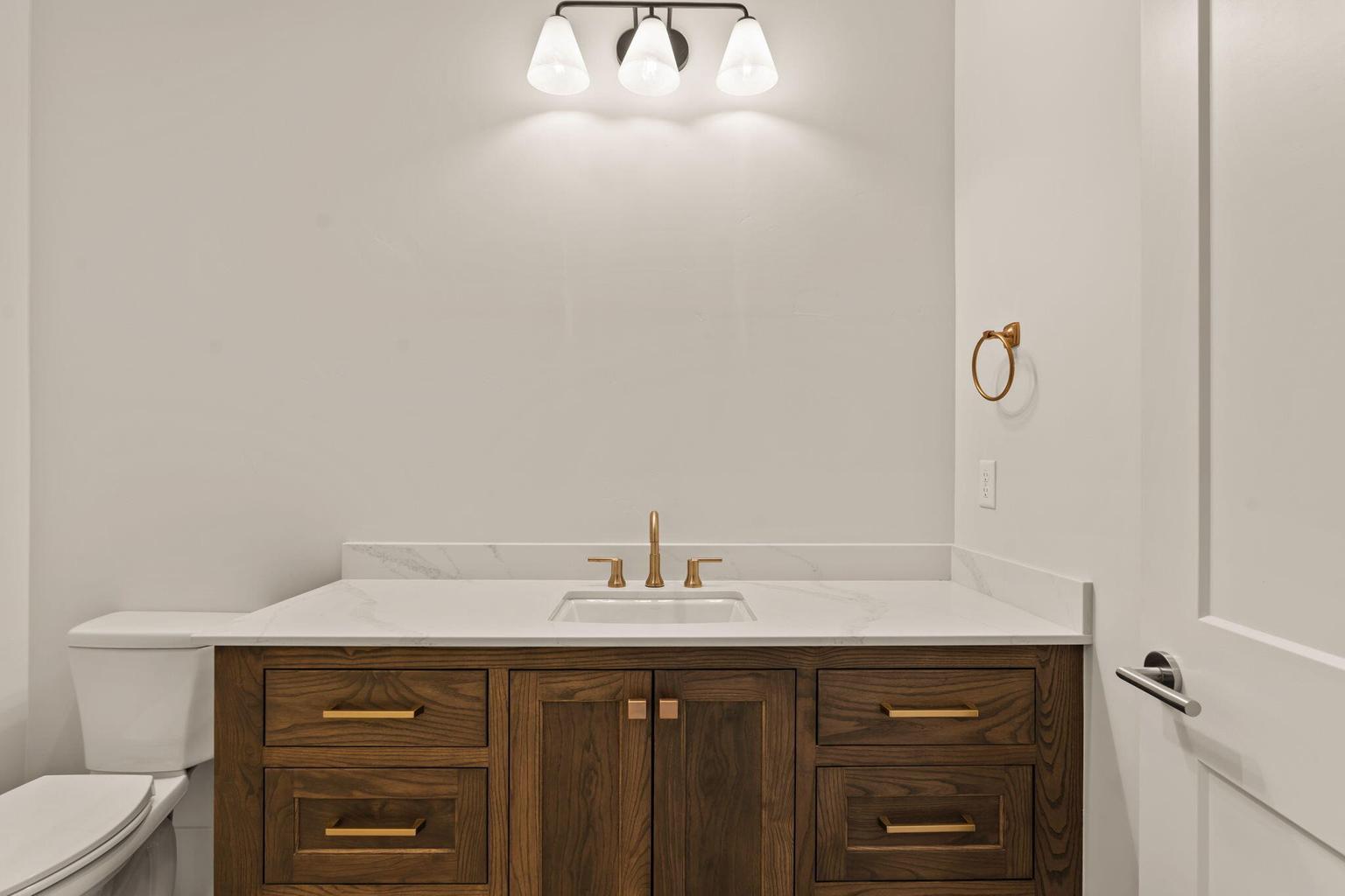 Bathroom vanity featuring a white countertop with integrated sink, dark wood-finish cabinetry, and gold-tone hardware