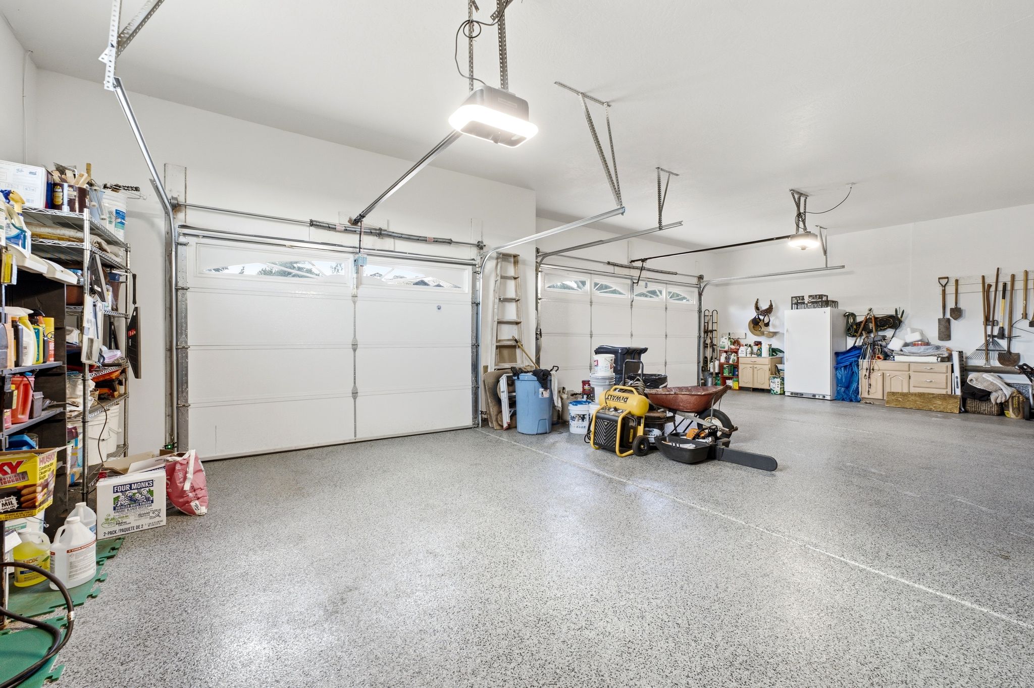 Spacious garage featuring a durable epoxy-coated concrete floor, two overhead garage doors with window inserts, and overhead lighting