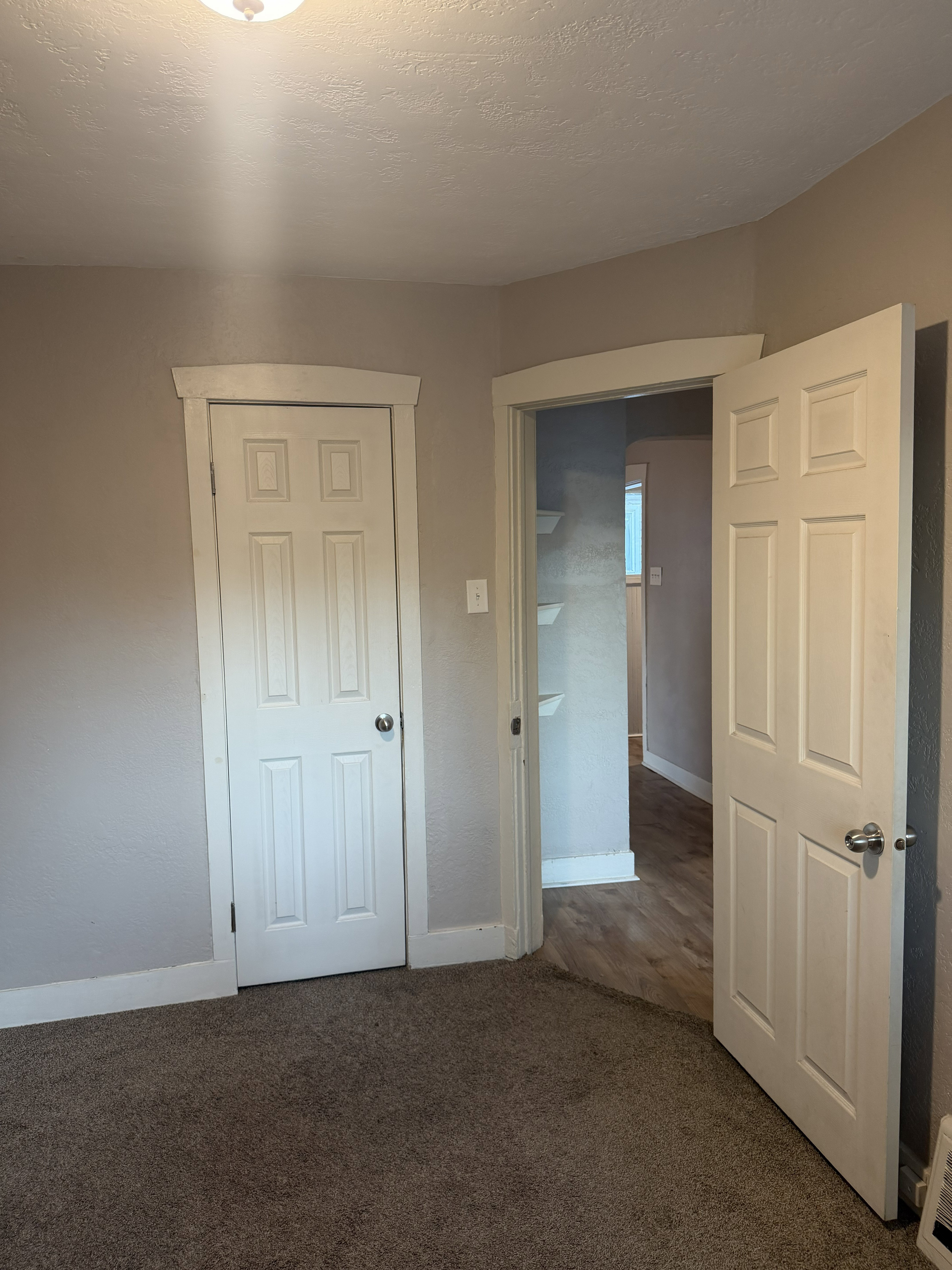 Neutral tone wall paint, textured ceiling, four-panel interior doors with white trim, and a ceiling-mounted light fixture