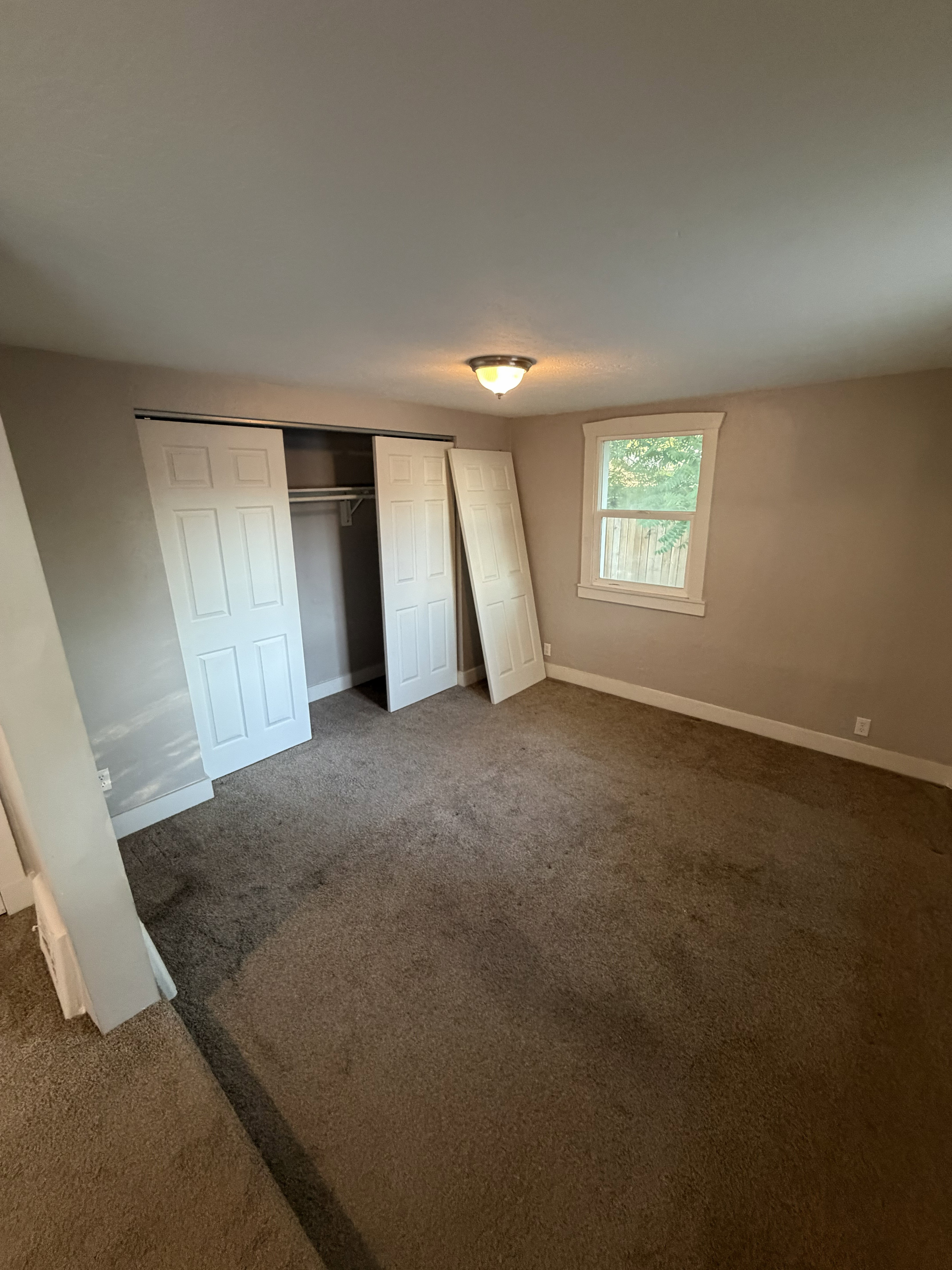 Carpeted room featuring a window with white trim, a flush mount ceiling light, and a closet with bifold doors