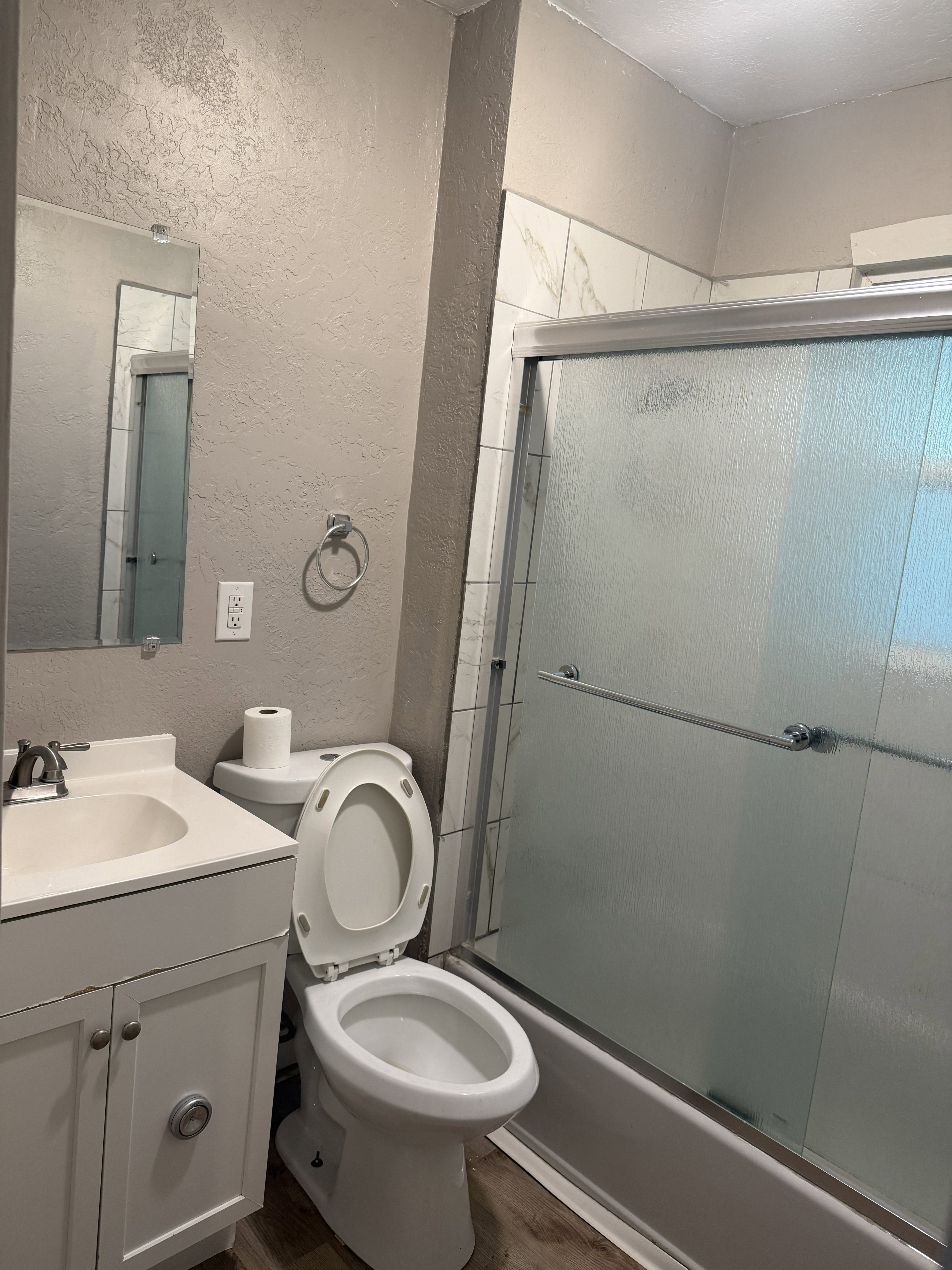 Bathroom featuring a white vanity with sink, a toilet, and a bathtub with a sliding glass door enclosure