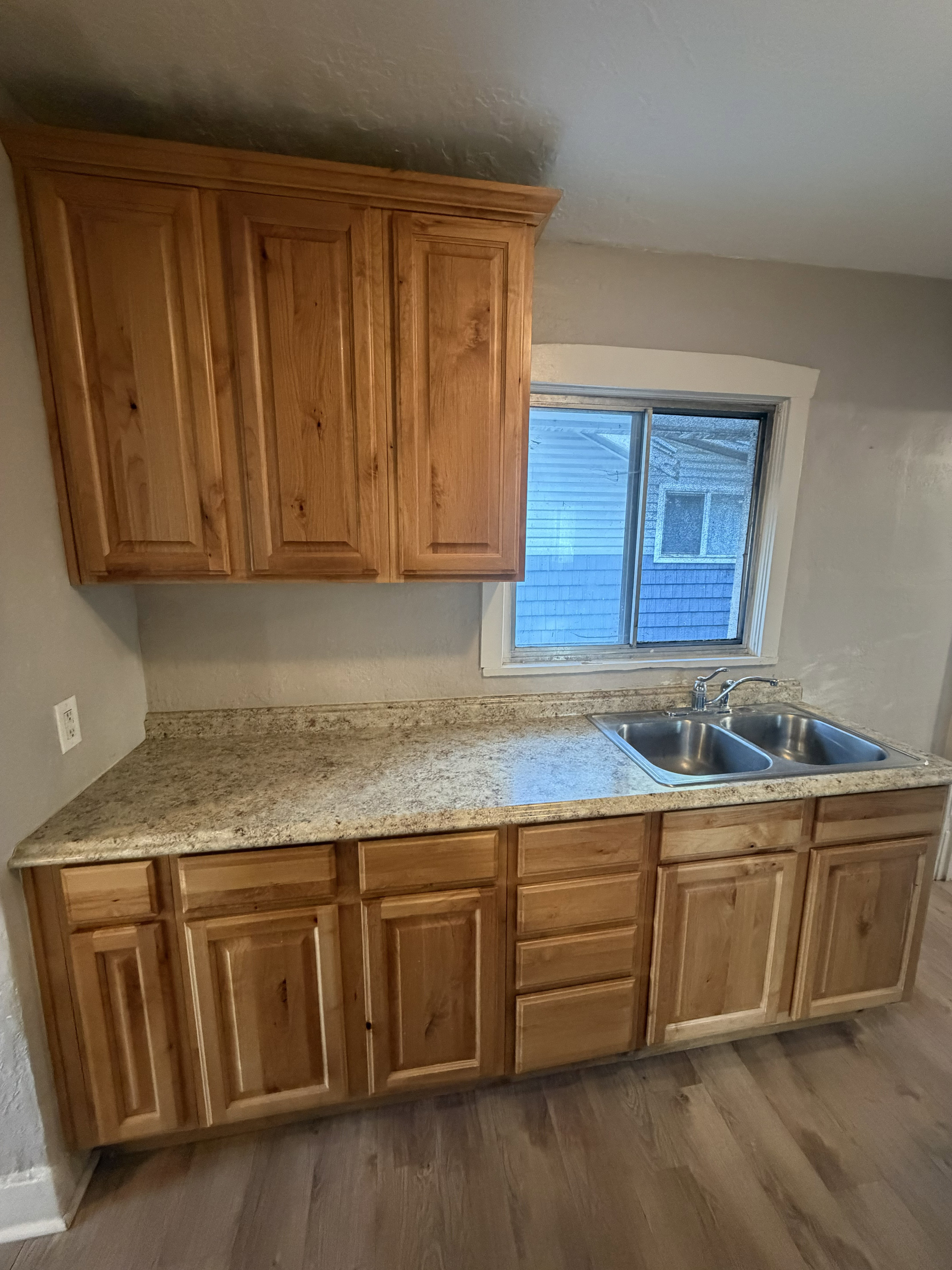 Kitchen area featuring light wood cabinetry with upper and lower storage, granite-look countertops, and a double-basin stainless steel sink