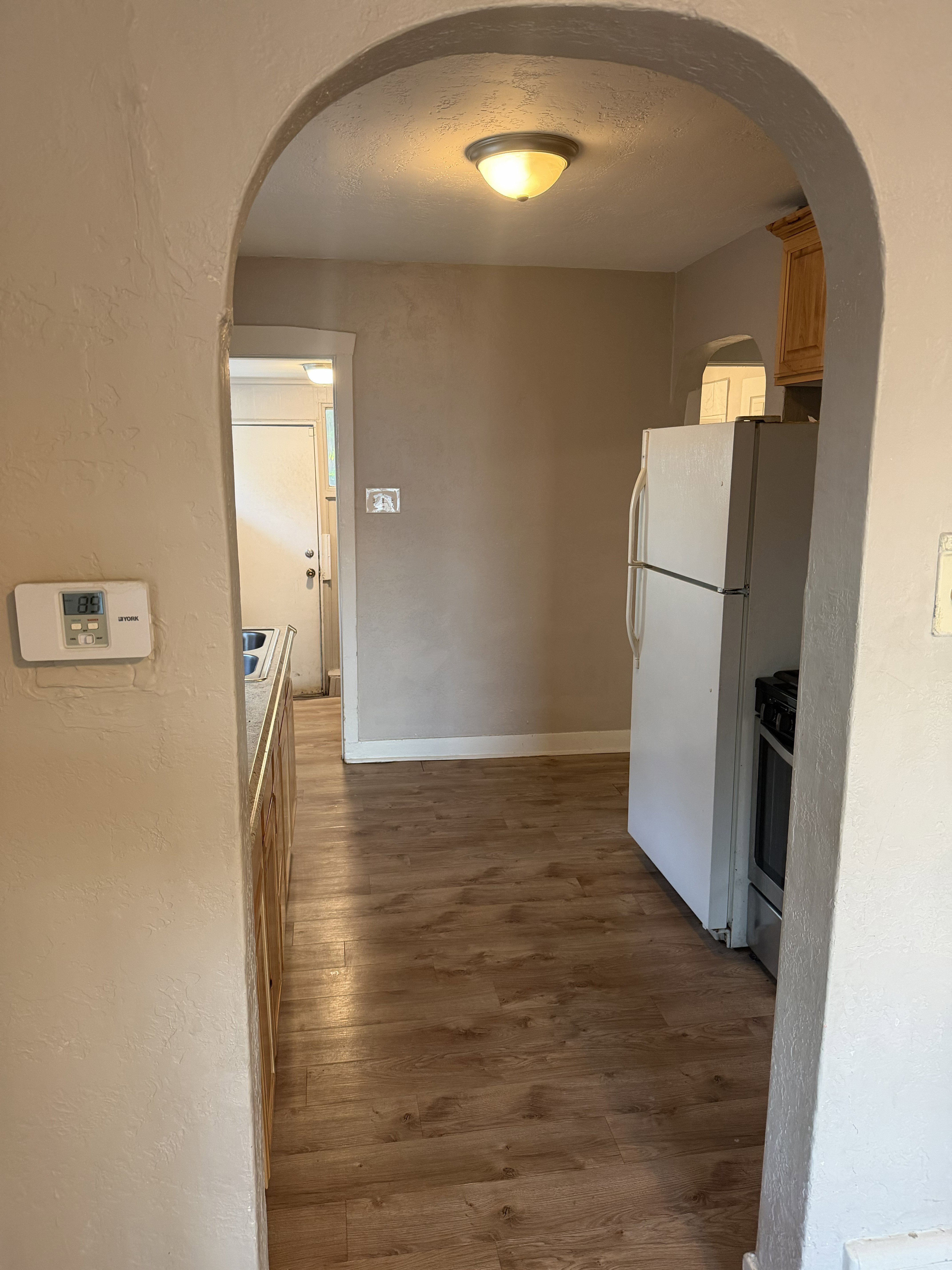 Archway entry to a room featuring wood-finish flooring, light tan wall paint, ceiling light fixture, and white trim