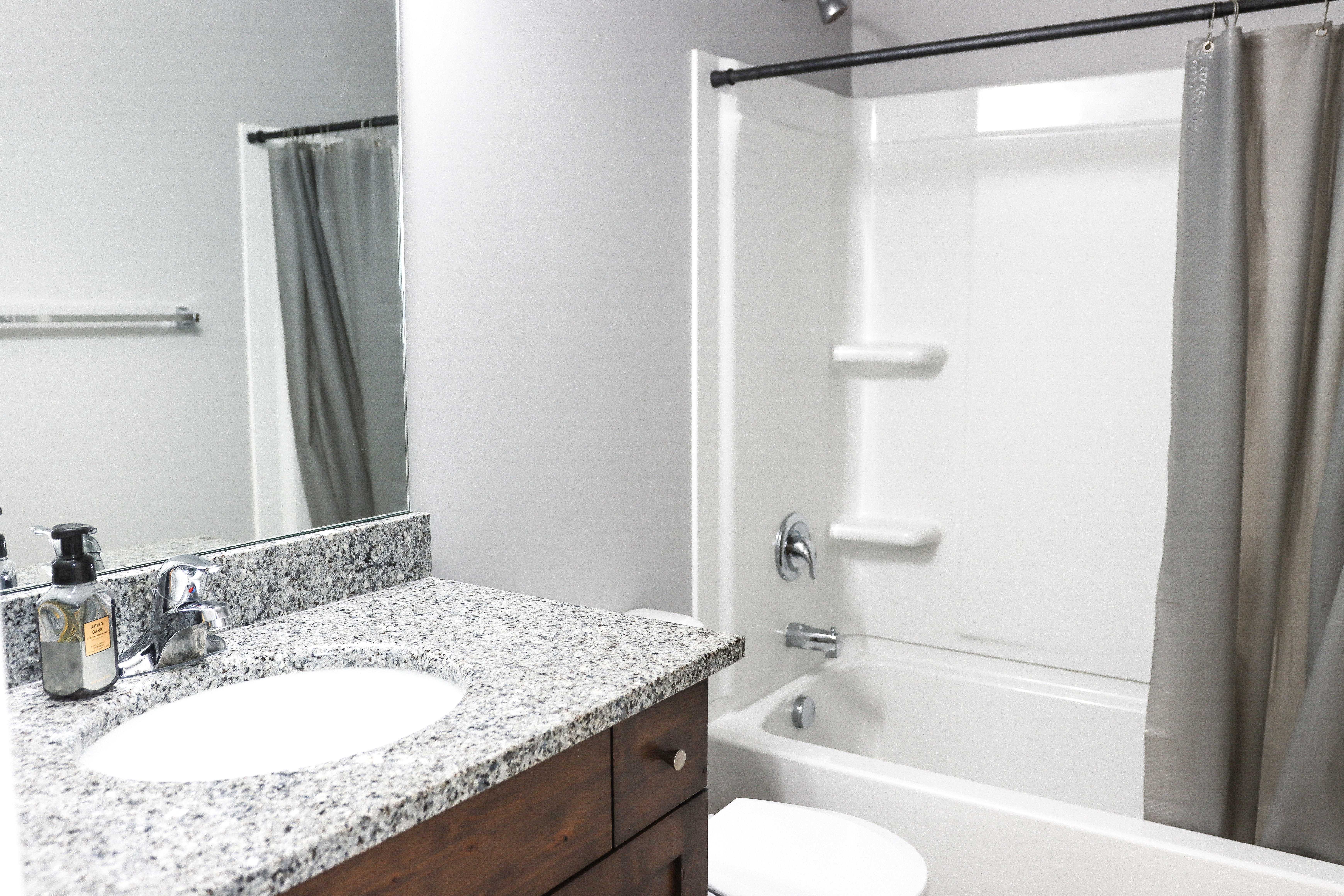 Full bathroom featuring a white tub/shower combination with chrome fixtures, a dark wood-finish vanity with a speckled countertop, and a built-in mirror