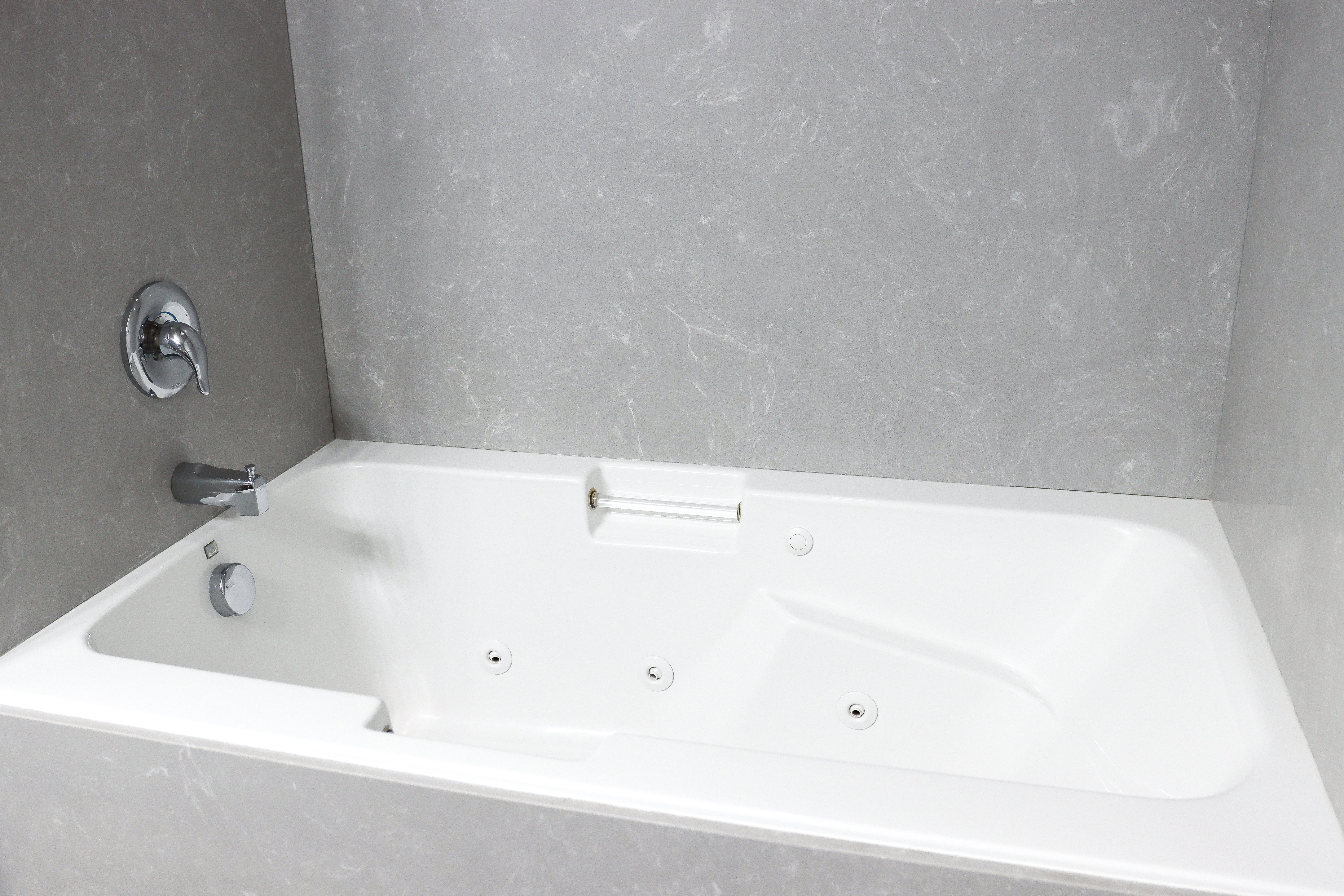 White jetted soaking tub with chrome fixtures and light gray patterned wall surround